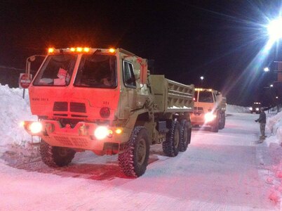 Tactical dump trucks from the Massachusetts National Guard's 181st Engineers from Joint Base Cape Cod gather at the local high school following state activation in response to record snowfalls over the past few weeks.