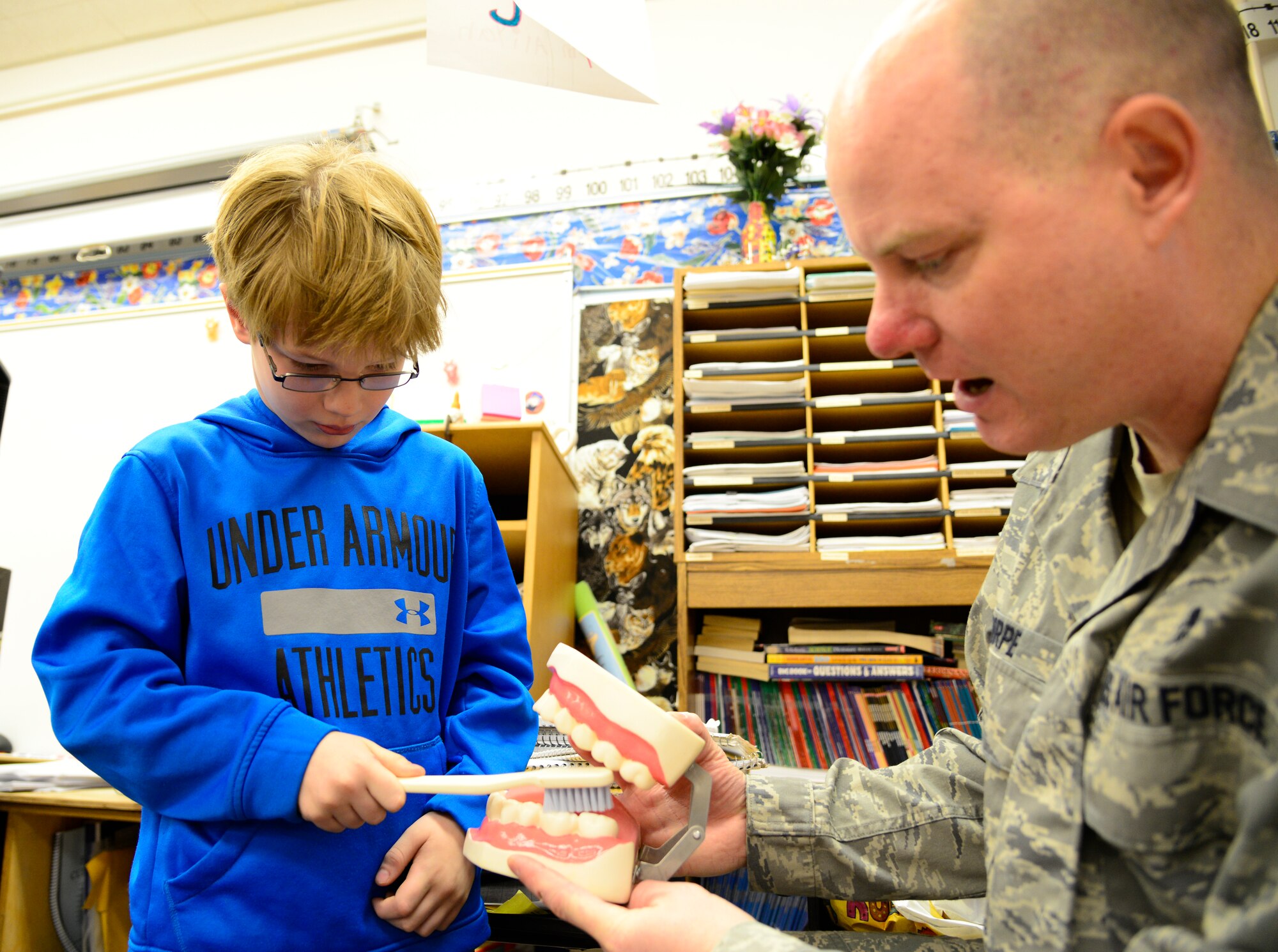 Brecken Thorpe, a dental health month participant, shows his father U.S. Air Force Master Sgt. Richard Thorpe, the 354th Medical Operations Squadron dental flight chief, how to brush during a National Children’s Dental Health month demonstration at Anderson Elementary, Eielson Air Force Base, Alaska, Feb. 10, 2015. Icemen from the dental office explained the importance of staying away from sugary foods, eating a healthy diet, how toothpaste is a vitamin for teeth and gave brushing and flossing techniques. (U.S. Air Force photo by Senior Airman Racheal E. Watson/Released)