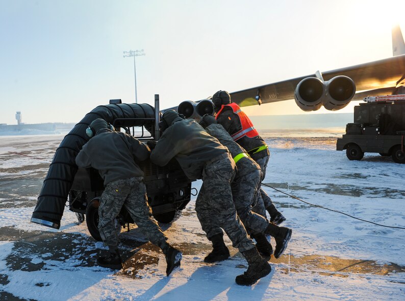 Crew chiefs from the 5th Aircraft Maintenance Squadron push a ground heater away from a B-52H Stratofortress on Minot Air Force Base, N.D., Feb. 4, 2015. The team ensured all ground equipment was away from the aircraft before preparing for takeoff. (U.S. Air Force photo/Senior Airman Stephanie Morris)