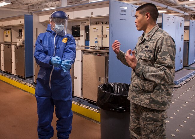 Col. John Lamontagne, 437th Airlift Wing commander, dons protective gloves during infection prevention and control practice while listening to procedures from Maj. Jason Okumura, 437th Aerial Port Squadron commander Feb. 5, 2015, at Joint Base Charleston – Air Base, S.C. The 437th AW leadership stopped by the 437th APS to learn more about personal protective equipment and its benefits during the event of an emergency.  (U.S. Air Force photo / Senior Airman Tom Brading)