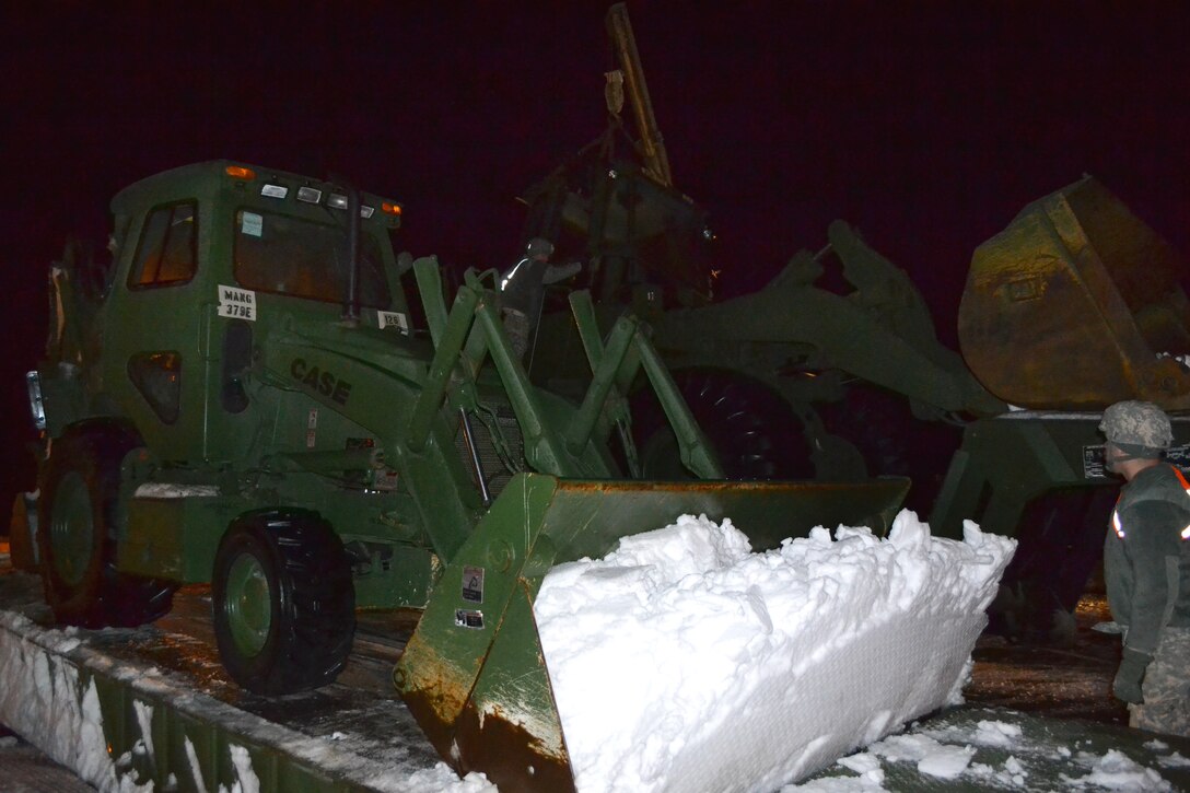 A soldier guides a bucket loader operator removing snow from a motor