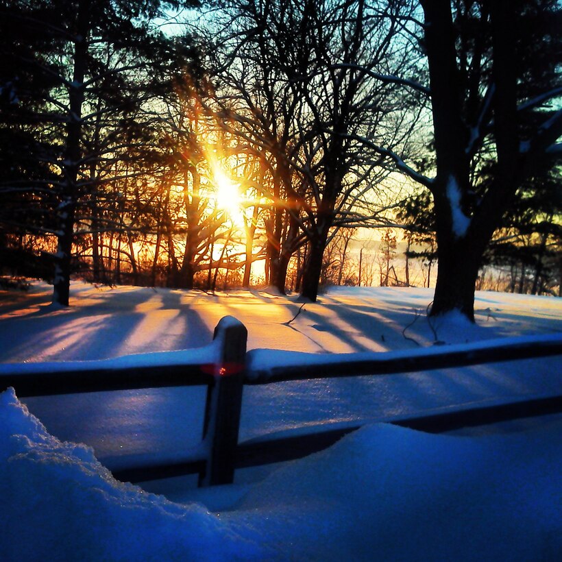 A frozen J. Edward Roush Lake is visible through the trees as the sun rises on a snowy morning in Huntington, Ind.