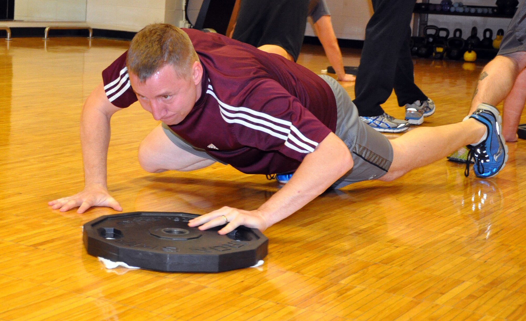 Capt. Brian Doom, a pilot assigned to the 18th Air Refueling Squadron, 931st Air Refueling Group, bear crawls across the floor while pushing a 45-pound plate during a group workout at the base fitness center, Feb. 4, 2015. Several members of the 18 ARS meet at the fitness center daily to participate in organized group workouts to improve overall unit fitness and to stay "fit to fight." (U.S. Air Force photo by Capt. Zach Anderson)
