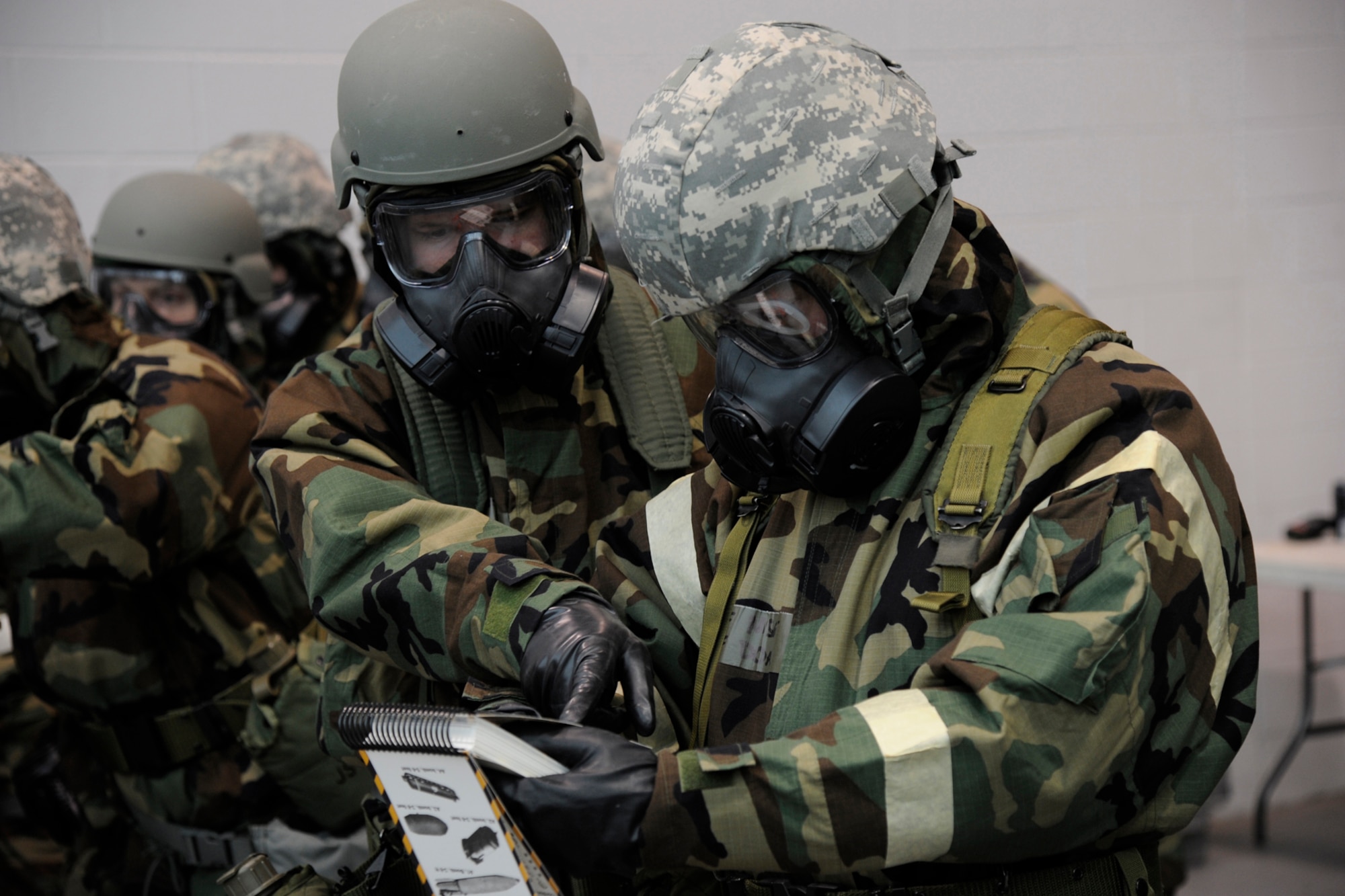 Two 127th Wing Airmen review information inside the Airman's Manual while dressed in Mission Oriented Protective Posture, or MOPP gear, during an expeditionary skills training day at Selfridge Air National Guard Base, Mich., Feb 8, 2015. Every three years, all airmen must attend expeditionary skills refresher training, in order to maintain their readiness.  (U.S. Air National Guard photo by Senior Amn. Ryan Zeski)