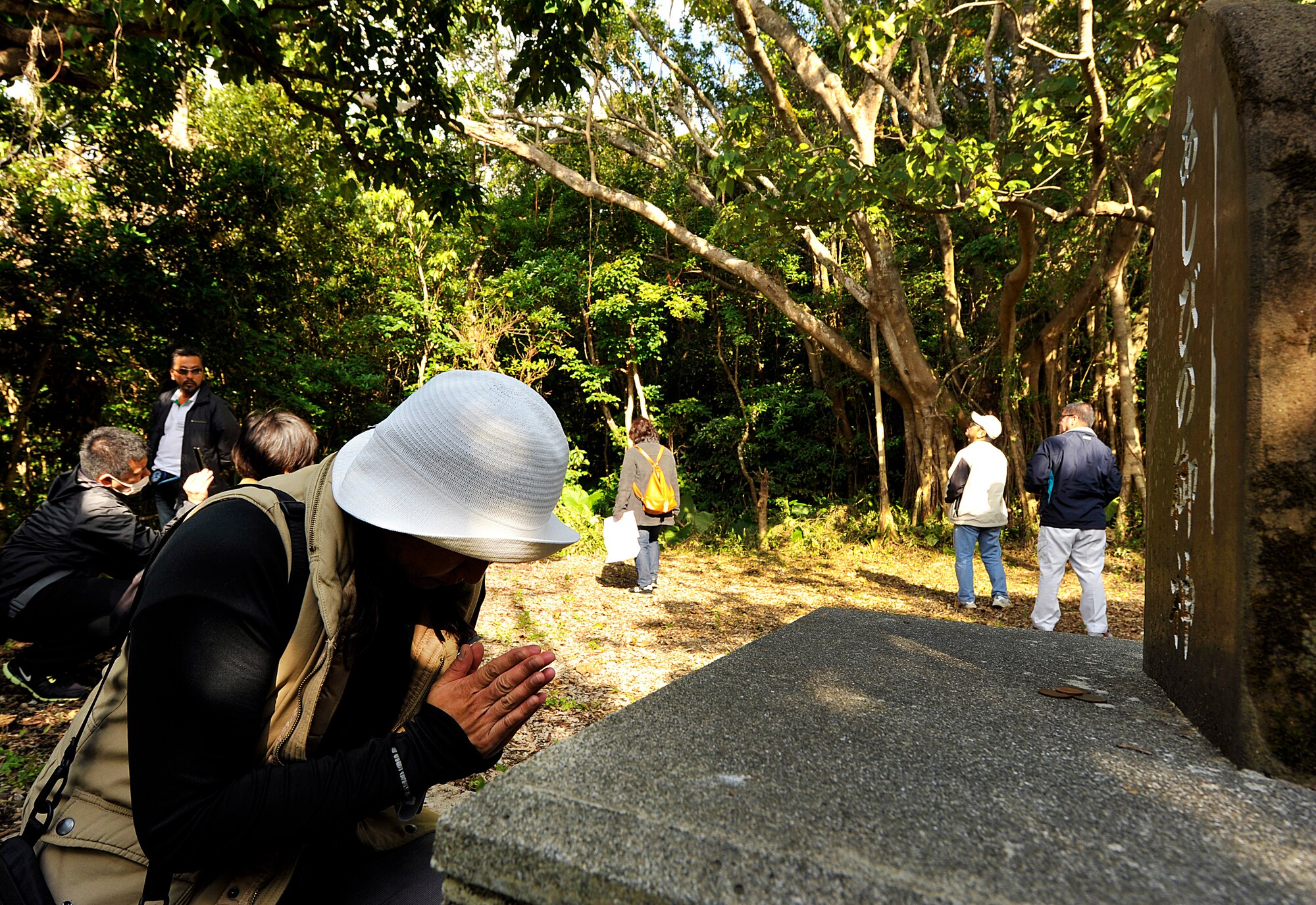 A woman from the Chatan Hometown Association prays after puting a coin in front of a tombstone at the Ashibi-na (playing square) on Kadena Air Base, Okinawa, Japan, Feb. 11, 2015. The Ashibi-na was used as a social gathering place for the villagers for about 40 years up until the year 1927, when a community hall was built. (U.S. Air Force photo by Naoto Anazawa)

