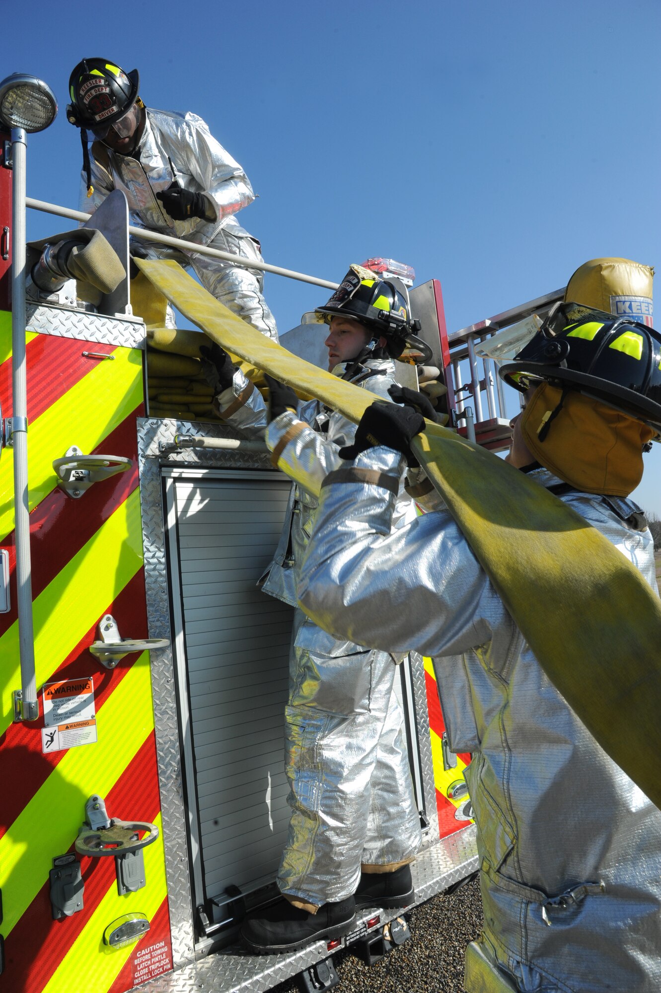 Senior Airman Jeffery Spivey, Staff Sgt. Joshua Hartwell and Senior Airman Aaron White, 81st Infrastructure Division firefighters, load a fire hose on to the truck after responding during a major accident response exercise Feb. 12, 2015, on the flight line, Keesler Air Force Base, Miss.  The MARE simulated a C-130J Hercules aircraft crash on base. The exercise was held to test the readiness of Keesler personnel during a major accident.  (U.S. Air Force photo by Kemberly Groue)