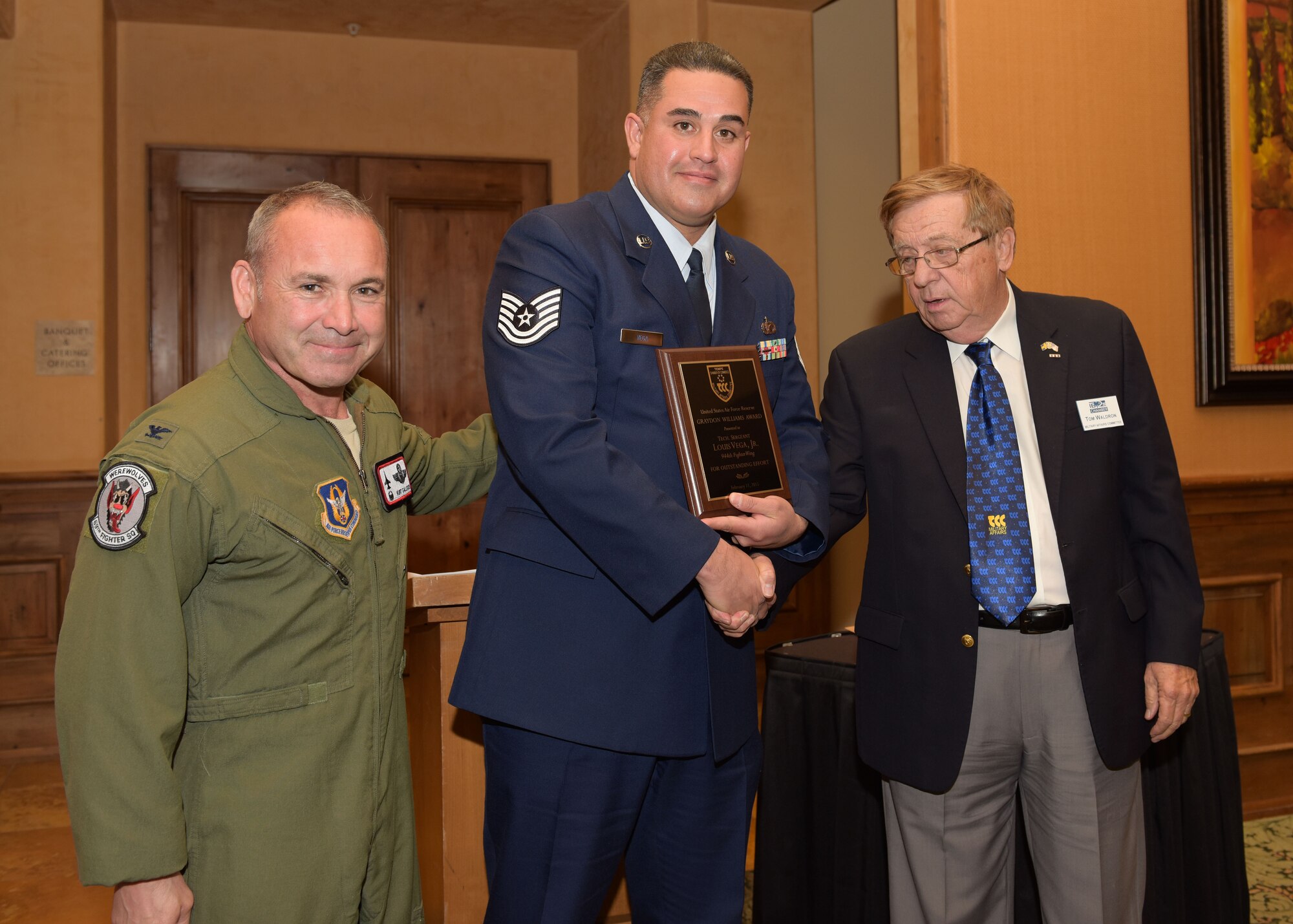 Tech. Sgt. Louis Vega Jr, 944th Fighter Wing public affairs specialist, receives the Graydon Williams Award from Mr. Thomas Waldron, co-chairman of the Tempe Military Affairs Committee and Col. Kurt Gallegos, 944th Fighter Wing commander Feb 11 at the Pebble Creek Country Club, Goodyear, Ariz. (U.S. Air Force photo by Staff Sgt. Lausanne Kinder)