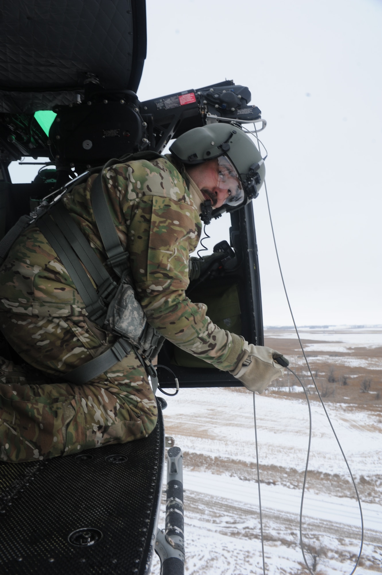 Tech. Sgt. Thomas Liscomb, 54th Helicopter Squadron flight engineer, lowers a hoist from a UH1-N helicopter near Minot Air Force Base, N.D., Feb. 11, 2015. Liscomb practiced his accuracy with a force penetrator hoist by lowering it into a barrel approximately 50 feet below the aircraft. (U.S. Air Force photos/Senior Airman Stephanie Morris)