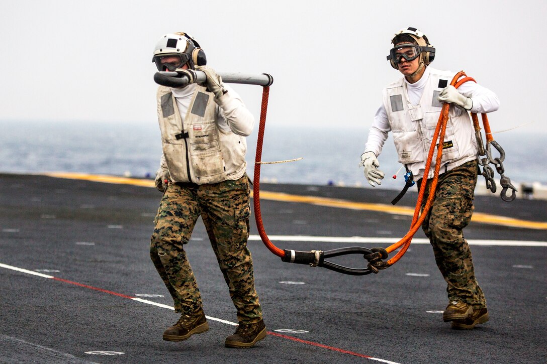 U.S. Marines carry a cargo strap off the flight deck aboard the USS Bonhomme Richard during a replenishment-at-sea with the USNS Washington Chambers in Aichi, Japan, Feb. 5, 2015.