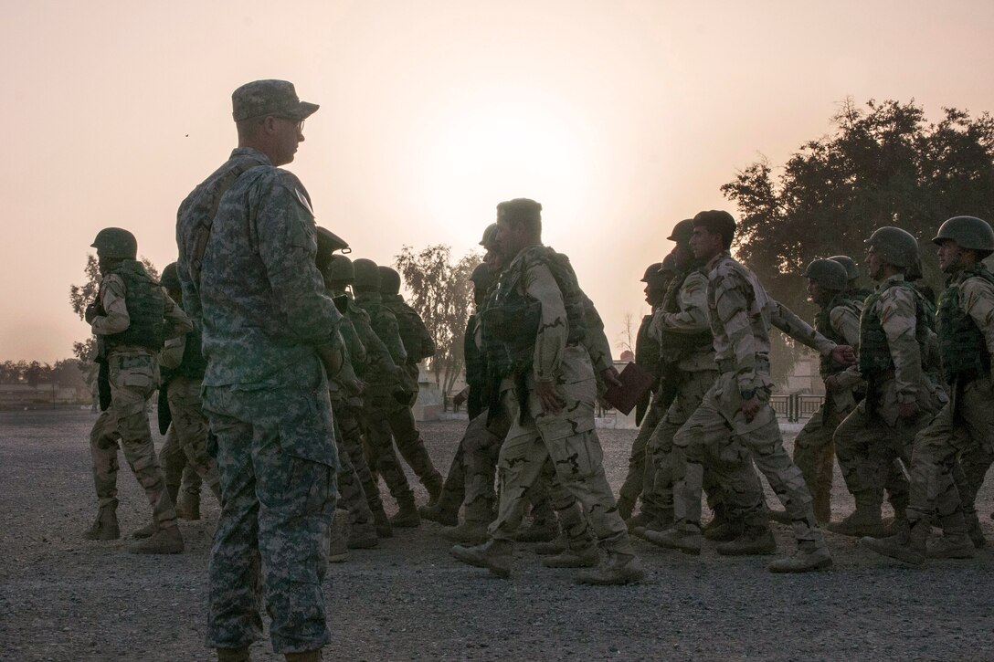 A U.S. Soldier watches as Iraqi army soldiers march on Camp Taji, Iraq, Feb. 13, 2015. The soldier is assigned to the 1st Infantry Division's 2nd Battalion, 34th Armor Regiment, 1st Armored Brigade Combat Team. More than 1,400 Iraqi trainees of the 72nd Iraqi Army Brigade graduated from a six-week training course, assisted by U.S. Soldiers, during a morning ceremony.