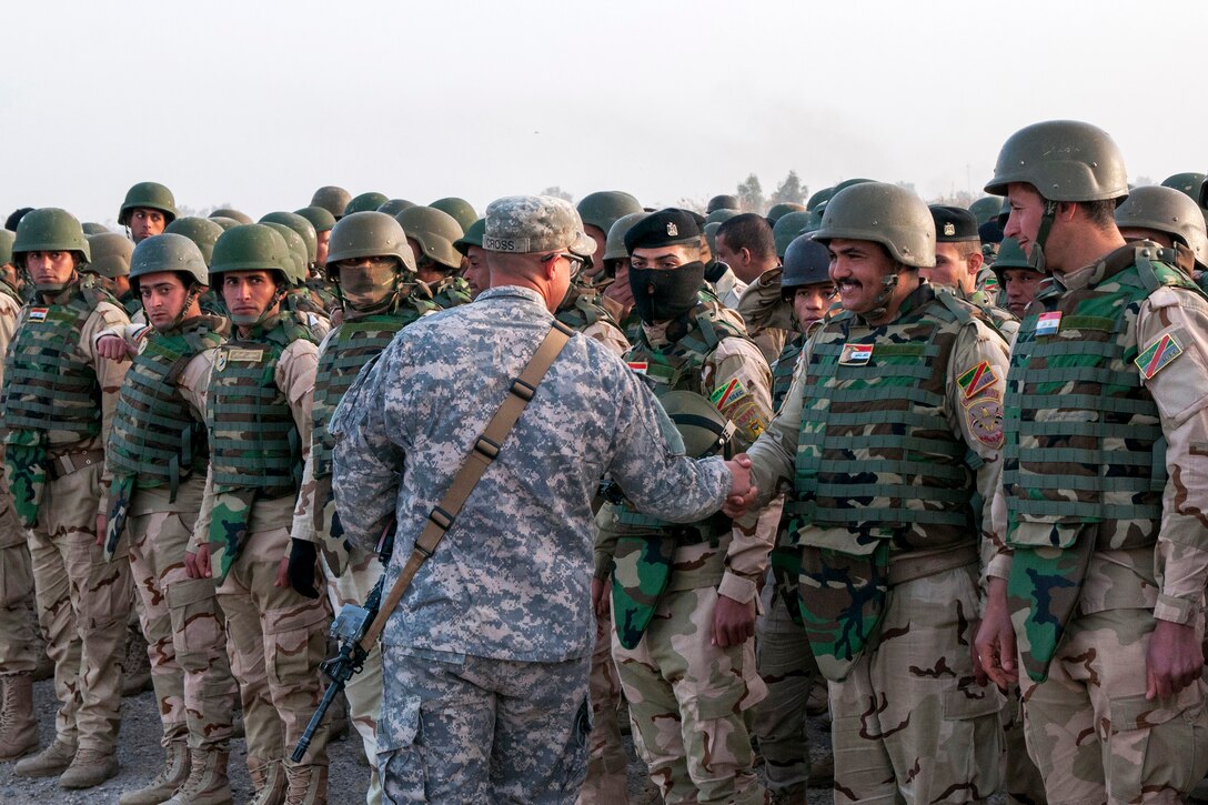 U.S. Army Staff Sgt. Kody Cross, center, congratulates Iraqi army trainees on their graduation ceremony from a six-week training course on Camp Taji, Iraq, Feb. 13, 2015. Cross is a squad leader assigned to the 1st Infantry Division's 2nd Battalion, 34th Armor Regiment, 1st Armored Brigade Combat Team.