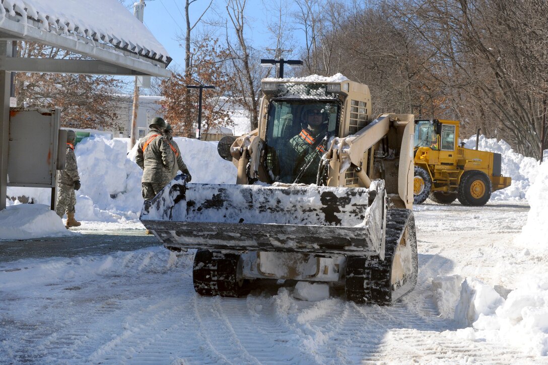 A guardsman operates a bulldozer to assist the local department of public works and Massachusetts Bay Transit Authority officials clear the parking lot during snow removal operations at the Bellevue Commuter Rail train station in West Roxbury, Mass., Feb. 16, 2015.