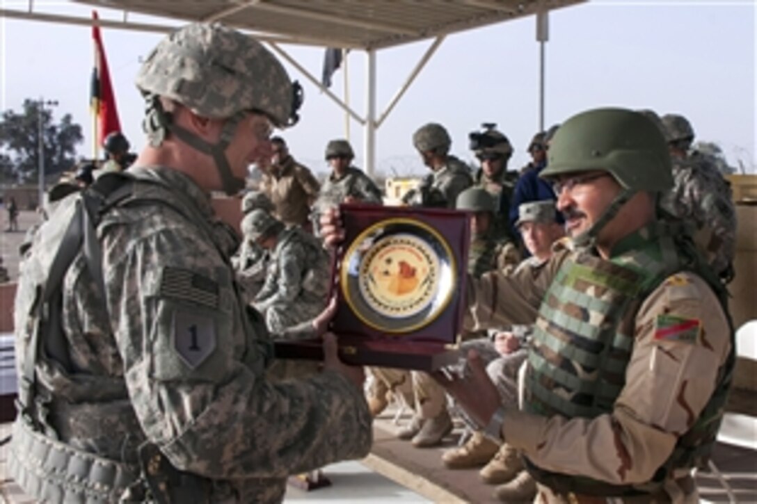 Iraqi Army Maj. Fahmy, right, presents a decorative plaque to U.S. Army Capt. John Cumbie and thanks him for his efforts in training more than 1,400 trainees during a graduation ceremony on Camp Taji, Iraq, Feb. 13, 2015. Cumbie commands the 1st Infantry Division's Company C, 2nd Battalion, 34th Armor Regiment, 1st Armored Brigade Combat Team. 