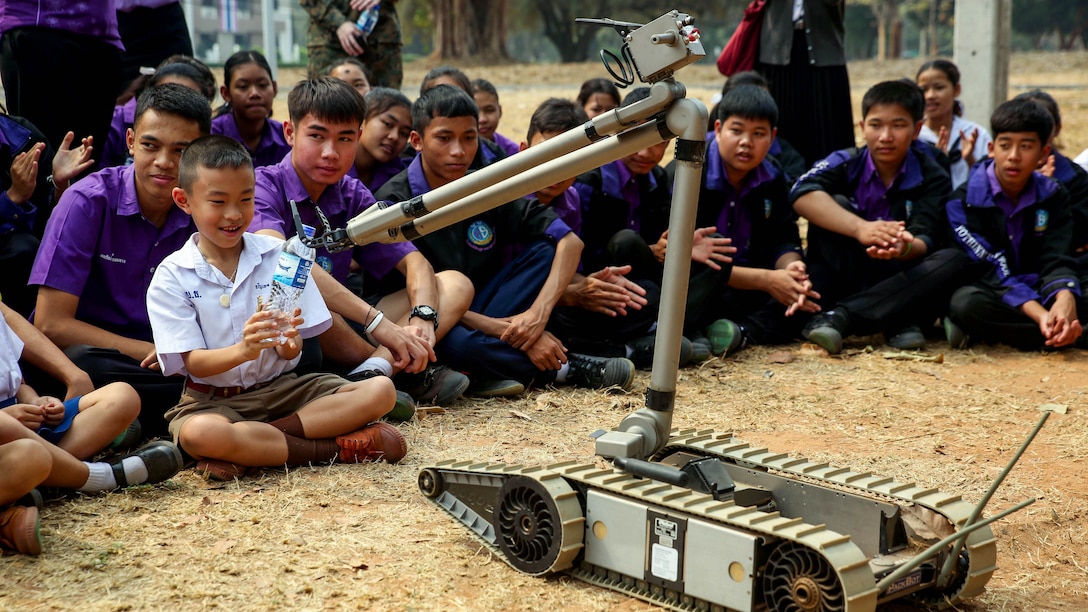 A student from Yothinnukun School receives a bottle of water from PackBot, a robot designed to carry out dangerous missions in high-threat battlefield scenarios, at Friendship Day held by Royal Thai Air Force Wing 1 and U.S. Marines at Royal Thai Air Force Base Korat during Exercise Cobra Gold 2015, Feb. 13. Students observed demonstrations of the Marine Corps Martial Arts Program, Explosive Ordnance Disposal, Aircraft Rescue Firefighting, and Navy Corpsmen basic medical procedures. Cobra Gold 2015 is a Thailand /United States co-sponsored, multinational and joint theater security cooperation exercise, conducted annually in the Kingdom of Thailand, with 25 nations participating. This year there is an increased focus on Humanitarian Civic Action, community engagement, and medical activities to support the needs and humanitarian interests of civilian populations around the region. 