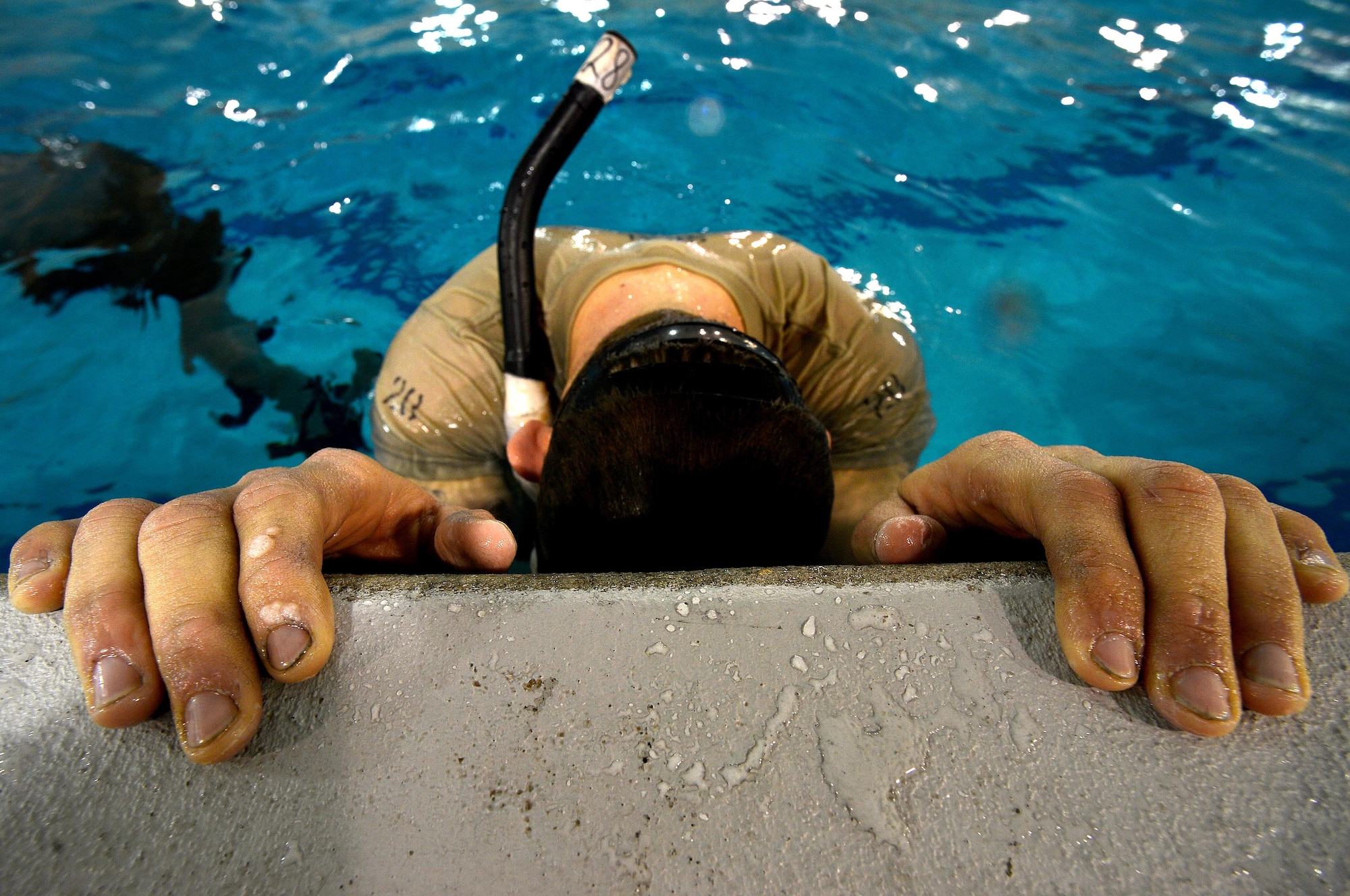 A U.S. Air Force Combat Control trainee assigned to Operating Location C, 342nd Training Squadron, hangs on to the side of the pool as he catches his breath and readies himself to swim more laps under water during an early morning water circuit training session at Pope Army Airfield, North Carolina, Feb 12, 2015. After the water circuits,  students were made to quickly get out of the pool and hustle to the gym for their next training session. (U.S. Air Force photo by Staff Sgt. Kenny Holston)