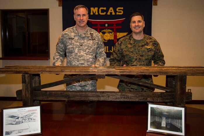 Army Col. John Hurley, left, the commanding officer of the U.S. Army Corps of Engineers, Japan District, and Col. Robert Boucher, the commanding officer of Marine Corps Air Station Iwakuni, Japan, pose in front of a restored bench inside Building One, aboard station, Feb. 4, 2015. The bench was presented to Boucher as part of a transfer of property ceremony with the intent to strengthen the bond between the two agencies. 