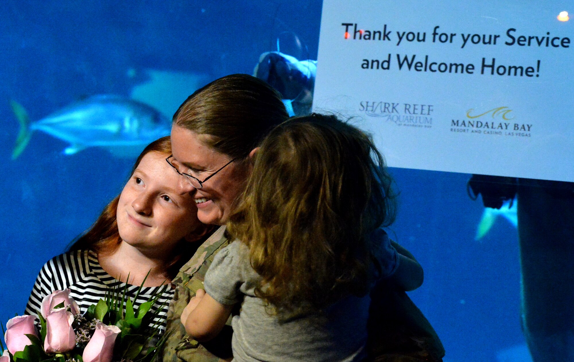 Staff Sgt. Julie Mauldin, a crew chief with the 432nd Aircraft Maintenance Squadron, hugs her daughters after surprising them with an early homecoming from a deployment to Southwest Asia, Feb. 13, 2015 at the Shark Reef Aquarium in Las Vegas. To add to the surprise, an  Aquarium scuba diver shared a sign thanking Mauldin for her service and welcoming her home. (U.S. Air Force photo by Senior Airman Adarius Petty/Released)