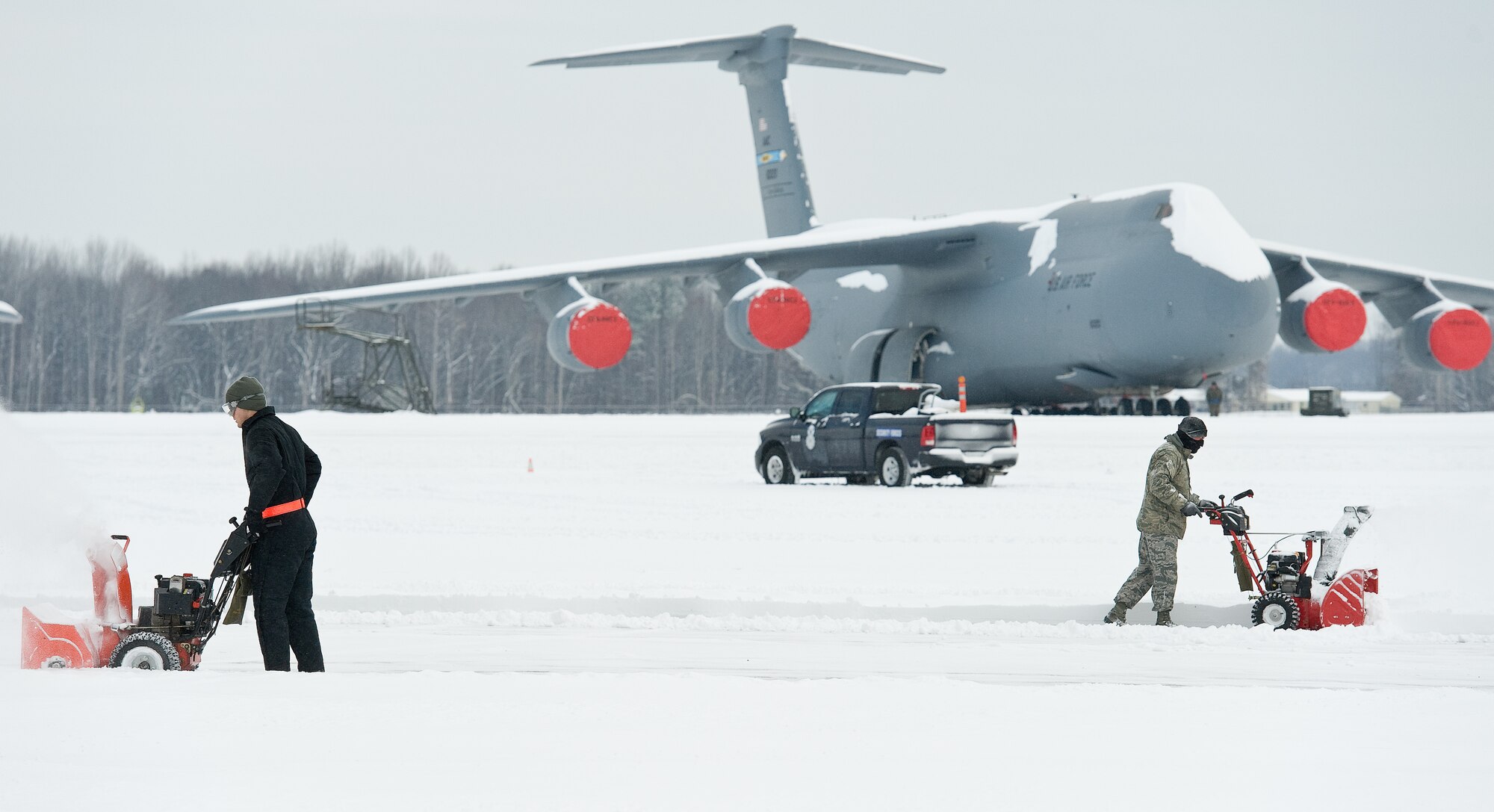 A C-5M Super Galaxy sits on the flight line as two Team Dover members use snow blowers to clear snow between two aircraft maintenance hangars Feb. 17, 2015, on Dover Air Force Base, Del. Winter Storm Octavia dumped a total of four inches of snow on the base and local area prompting wing leadership to initiate a two-hour reporting delay for Mission Essential Level 2 and 3 personnel. (U.S. Air Force photo/Roland Balik)