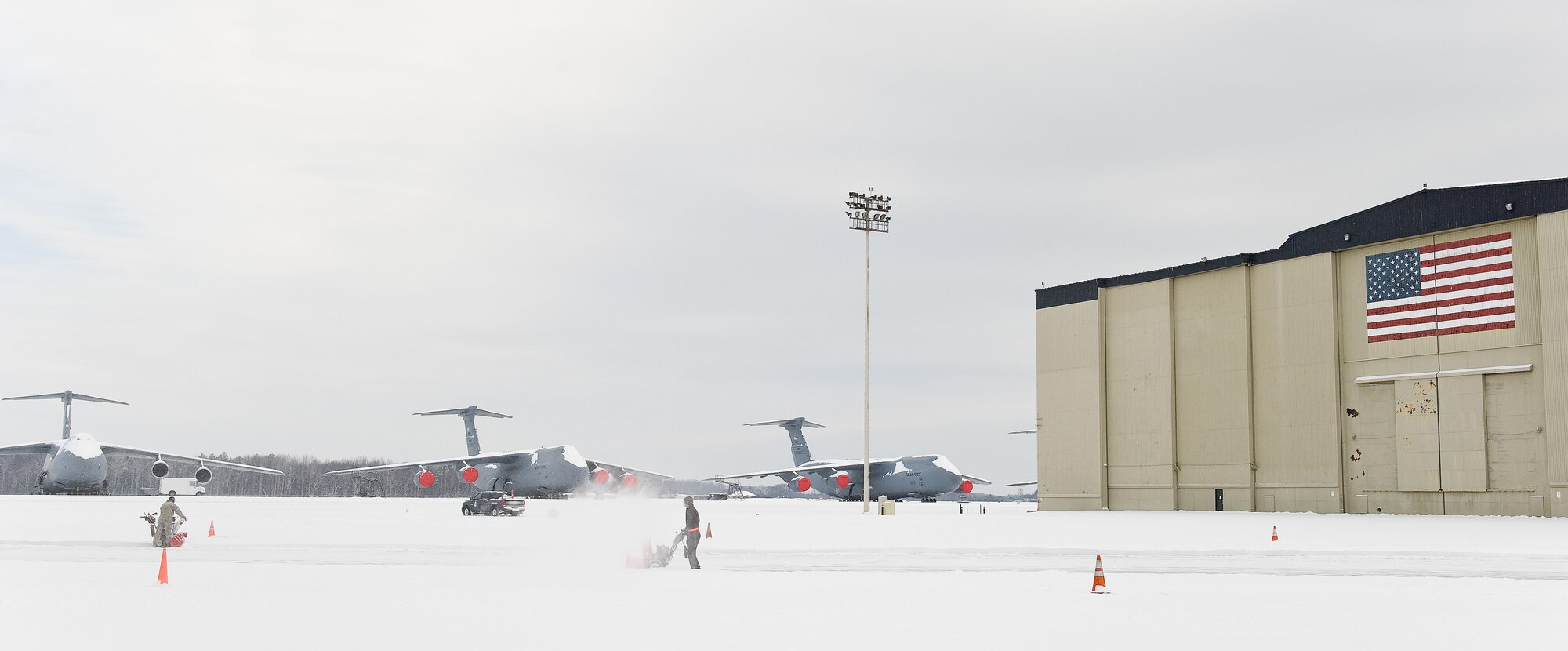 Three snow-covered C-5M Super Galaxies sit on the flight line as two Team Dover members clear snow from the north side of the C-5 Isochronal Inspection hangar Feb. 17, 2015, on Dover Air Force Base, Del. Base personnel kept the base operational by clearing four inches of snow from sidewalks, roads, parking lots, flight line, runways and taxiways. (U.S. Air Force photo/Roland Balik)