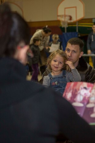Maj. Donald Hall, future operations officer the Marine Aircraft Group 12, and his daughter listen to a reading of “Cupig’s Scuffle” inside the Matthew C. Perry Elementary School gymnasium during M.C. Perry’s Family Literature Night, Feb. 12, 2015. The purpose of literature night is to bring families aboard the air station together by sparking an interest in reading by utilizing interactive stations. 