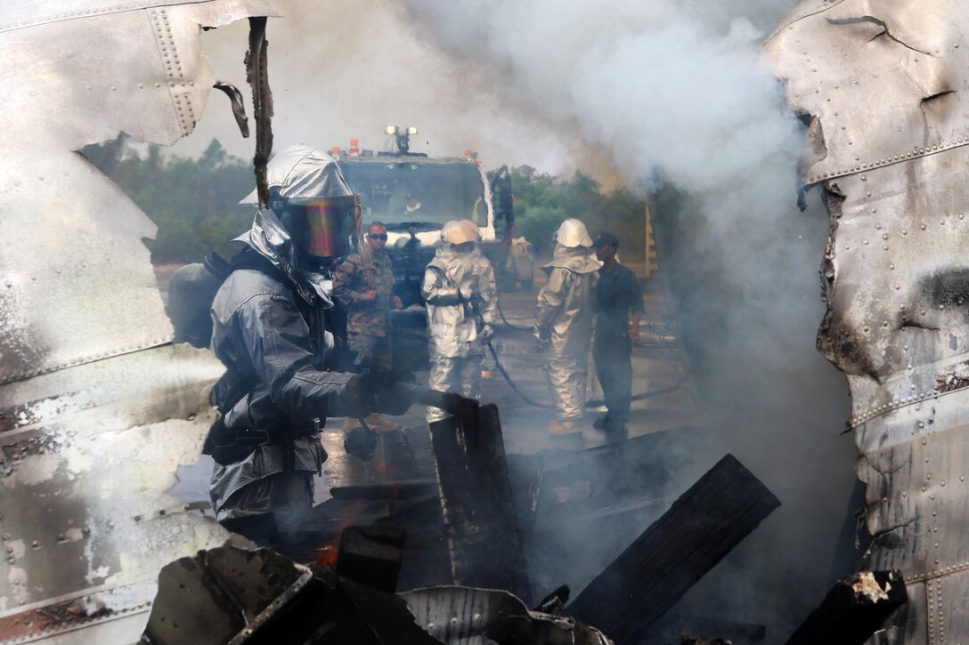 U.S. Marine Corps Cpl. Justin Groom stokes the fire inside of a scrap airplane during a fire response scenario to ensure it is completely out on Utapao Royal Thai Navy Airfield, Kingdom of Thailand, Feb 18, 2015. 