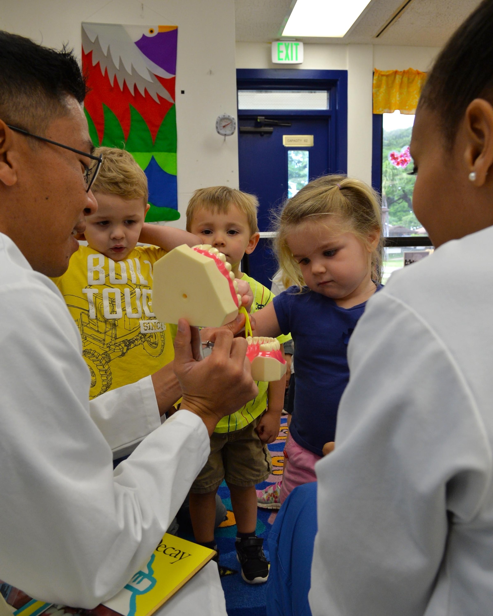 Capt. Evan Masunaga (Left) and Staff Sgt. Britney Jones both from the 15th Aerospace Medicine Squadron demonstrate proper oral hygiene to students at the Main Child Development Center on Joint Base Pearl Harbor-Hickam, Hawaii, Feb. 19, 2015. Masunaga and Jones delivered their message of oral hygiene through activities with oversized teeth and toothbrushes, along with gift bags containing two-minute teeth brushing timers, a toothbrush and sugar free lollipops. (U.S. Air Force photo by Tech. Sgt. Aaron Oelrich/Released) 