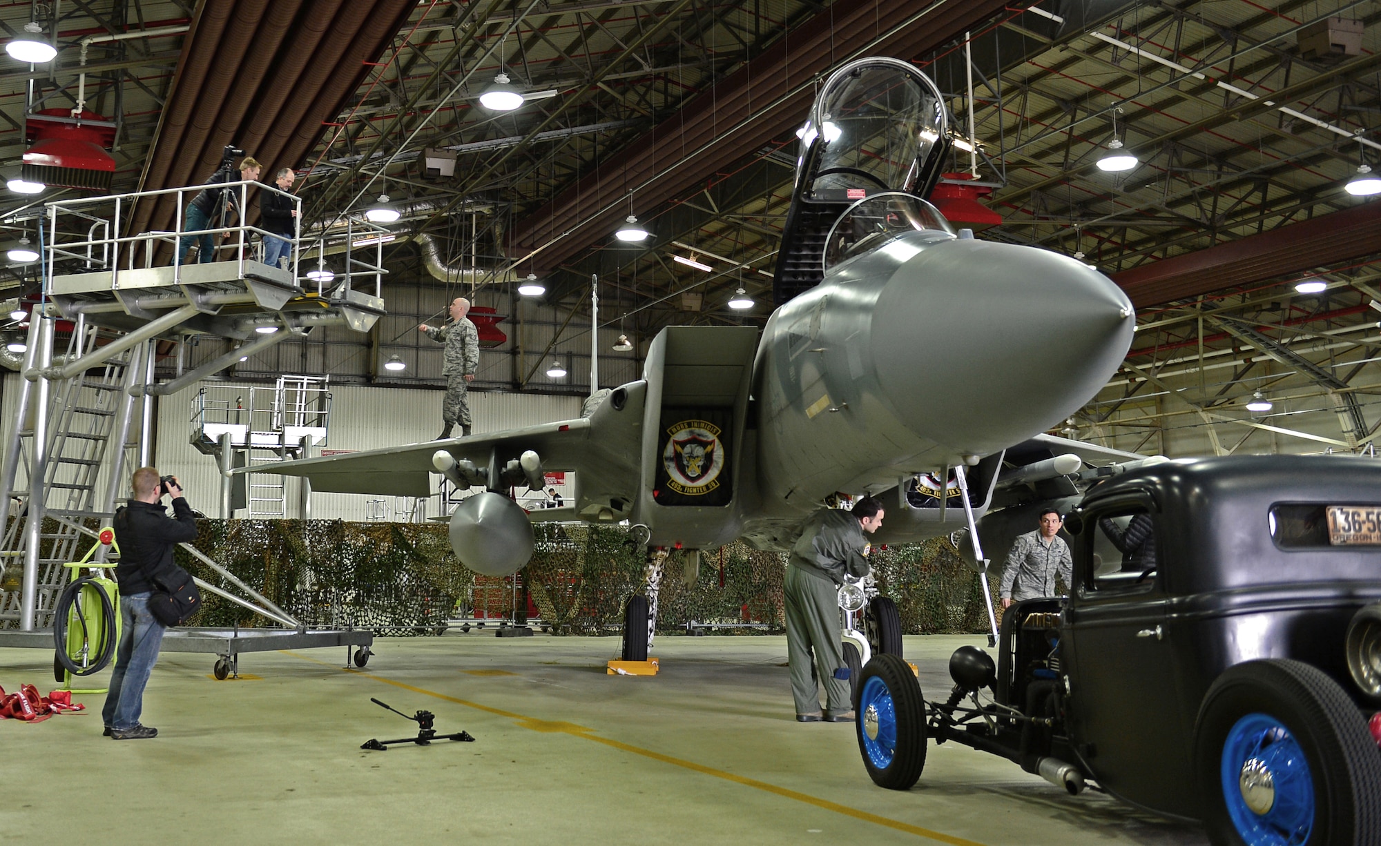 James Lipman, freelance photographer (top left), communicates with Tech. Sgt. Ryan Forsse, 492nd Aircraft Maintenance Unit flightline expeditor, to get Hangar 7 set up for the BBC Top Gear Magazine photo shoot at Royal Air Force Lakenheath, England, Feb. 19, 2015. Media visited the 48th Fighter Wing to put together a feature about Liberty Airmen and their cars. (U.S. Air Force photo by Airman 1st Class Erin R. Babis/Released)