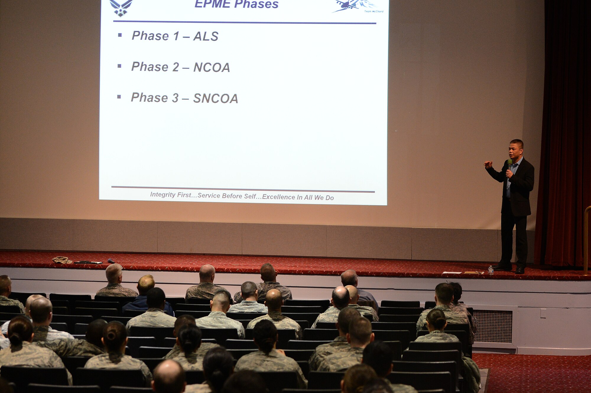 Mr. Eli Yamzon (on stage), 62nd Airlift wing formal training technician, briefs senior NCOs and NCOs at a formal training town hall conducted at the McChord Field Theater, Joint Base Lewis-McChord, Wash., Feb. 19, 2015. More than 200 members came out to listen to the changes in the Enlisted Professional Military Education for progression in the enlisted ranks. (U.S. Air Force photo/Staff Sgt. Tim Chacon)