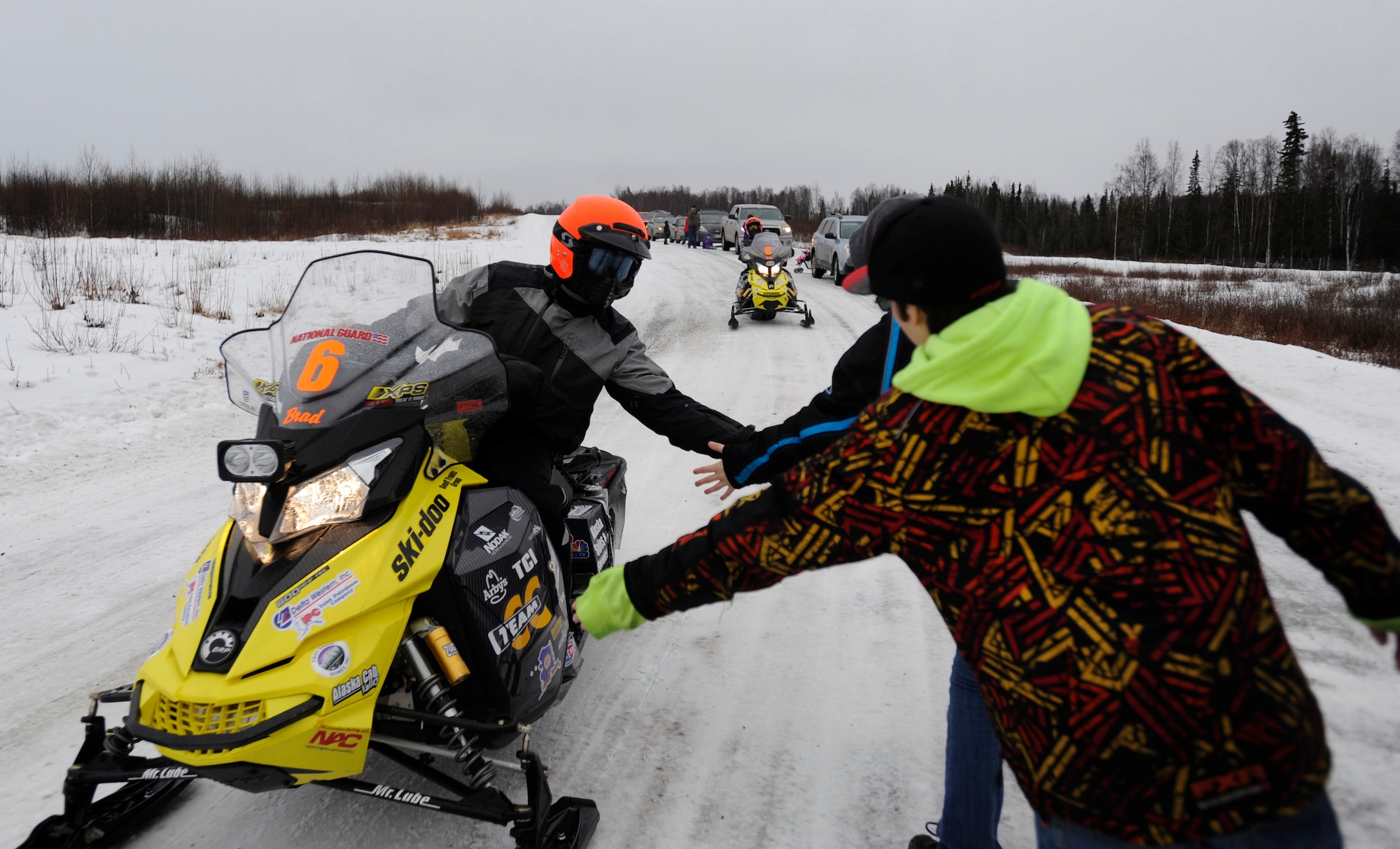 Children of the Roach family touch an Iron Dog racer as he passes on Joint Base Elmendorf-Richardson, Alaska, Feb. 21. The family are fans of the races and have participated in several events, including driving snow machines themselves. The Roaches are native of Lacon, Illinios. (U.S. Air Force photo/Tech. Sgt Robert Barnett)