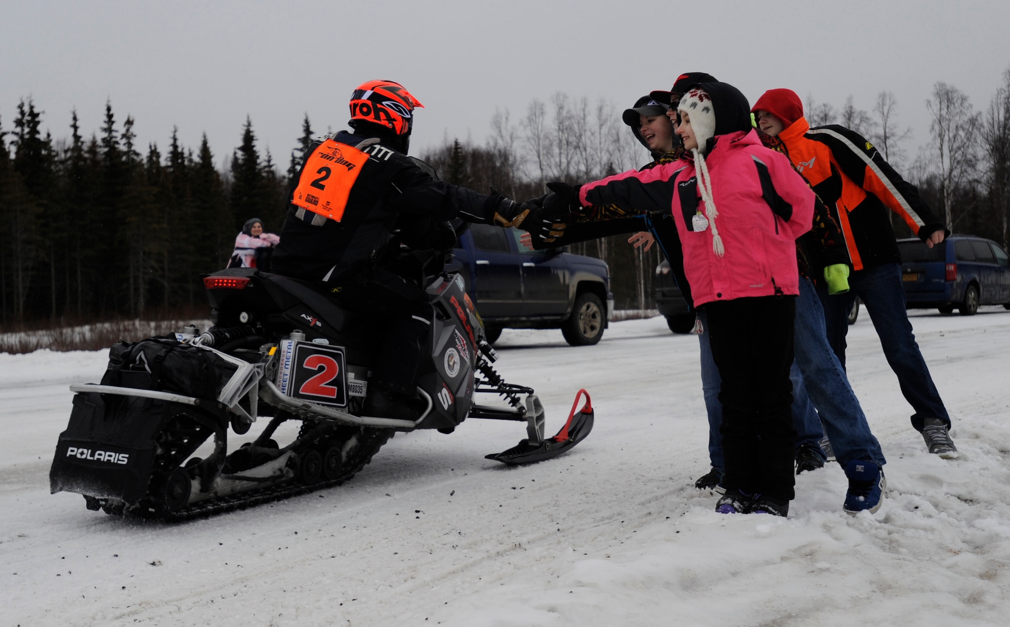 Children of the Roach family touch an Iron Dog racer as he passes on Joint Base Elmendorf-Richardson, Alaska, Feb. 21. The family are fans of the races and have participated in several events, including driving snow machines themselves. The Roaches are native of Lacon, Illinios. (U.S. Air Force photo/Tech. Sgt Robert Barnett)
