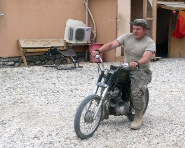 Spc. Skyler W. Genest a military policeman assigned to Troop B, 1-172nd Calvary Squadron, 86th Infantry Brigade Combat Team (Mountain) of the Vermont National Guard, takes his project bike for a ride, April 13, 2010. Genest found this project bike in the back of a storage bunker and decided to spend some of his free time fixing it up. Genest is an admitted tinkerer back home likes the challenge of trying to fix a 40-year-old motorcycle. He is quick to point out the .50 caliber ammunition box that he modified to be the gas tank.