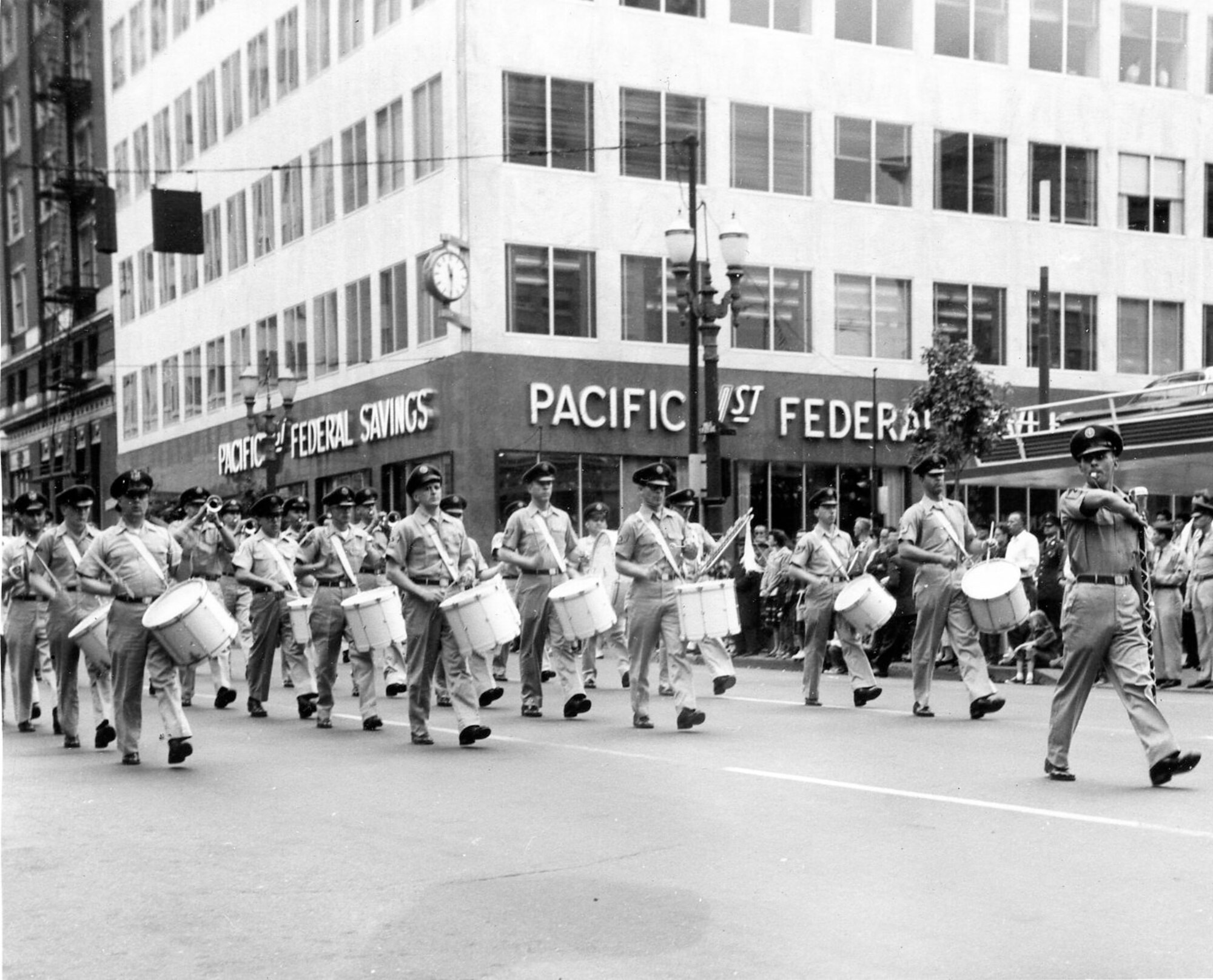 The OreANG’s Twirler, probably champion Ms. Carol Johnson, leads the OreANG Drum & Bugle Corps in the summer khaki uniforms of that era down a Portland street in the 53rd Annual Rose Festival’s Grand Floral Parade, Saturday, June 10, 1961. Drum Major MSgt Unverricht leads the corps immediately behind her.