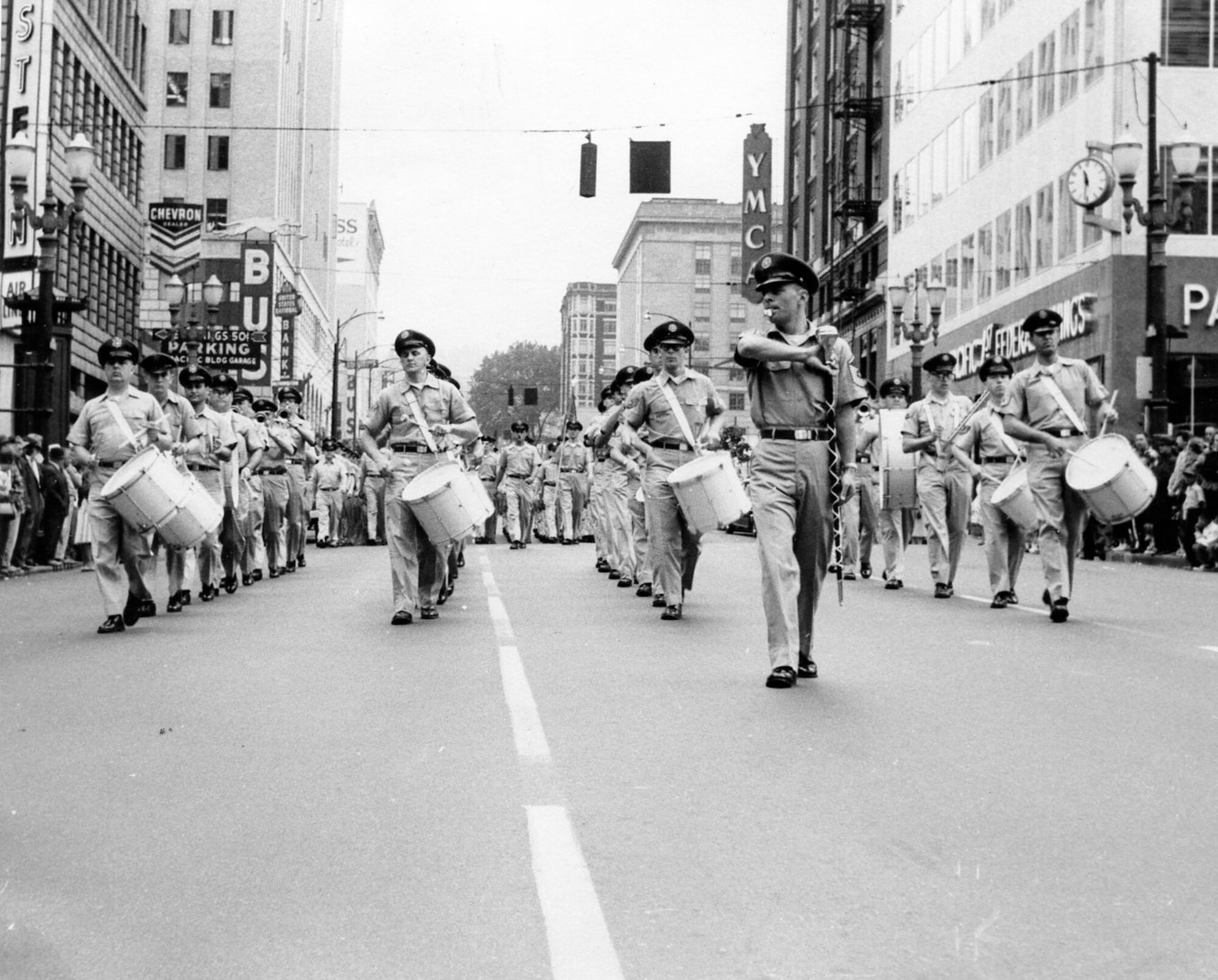 The OreANG’s Drum & Bugle Corps performed in the 11th Annual Armed Forces Day Parade on Saturday, May 20, 1961, seen here as the corps passes the reviewing stand (out of sight to left) in downtown Portland, Oregon, outside the Pioneer Post Office. The parade featured some 1,400 marchers and covered a route of 18 blocks.