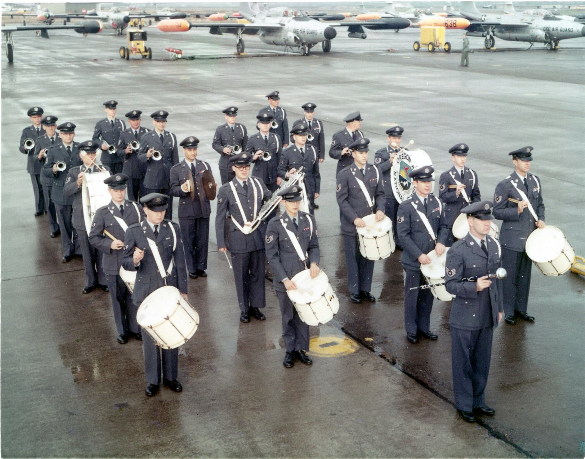 Members of the Oregon ANG (OreANG) Drum & Bugle Corps enjoy a moment in the sun as they stand ready on the ramp at Portland AFB in this early view of the corps, circa late 1960. Note the OreANG’s Northrop F-89J Scorpion fighter-interceptors in the background.