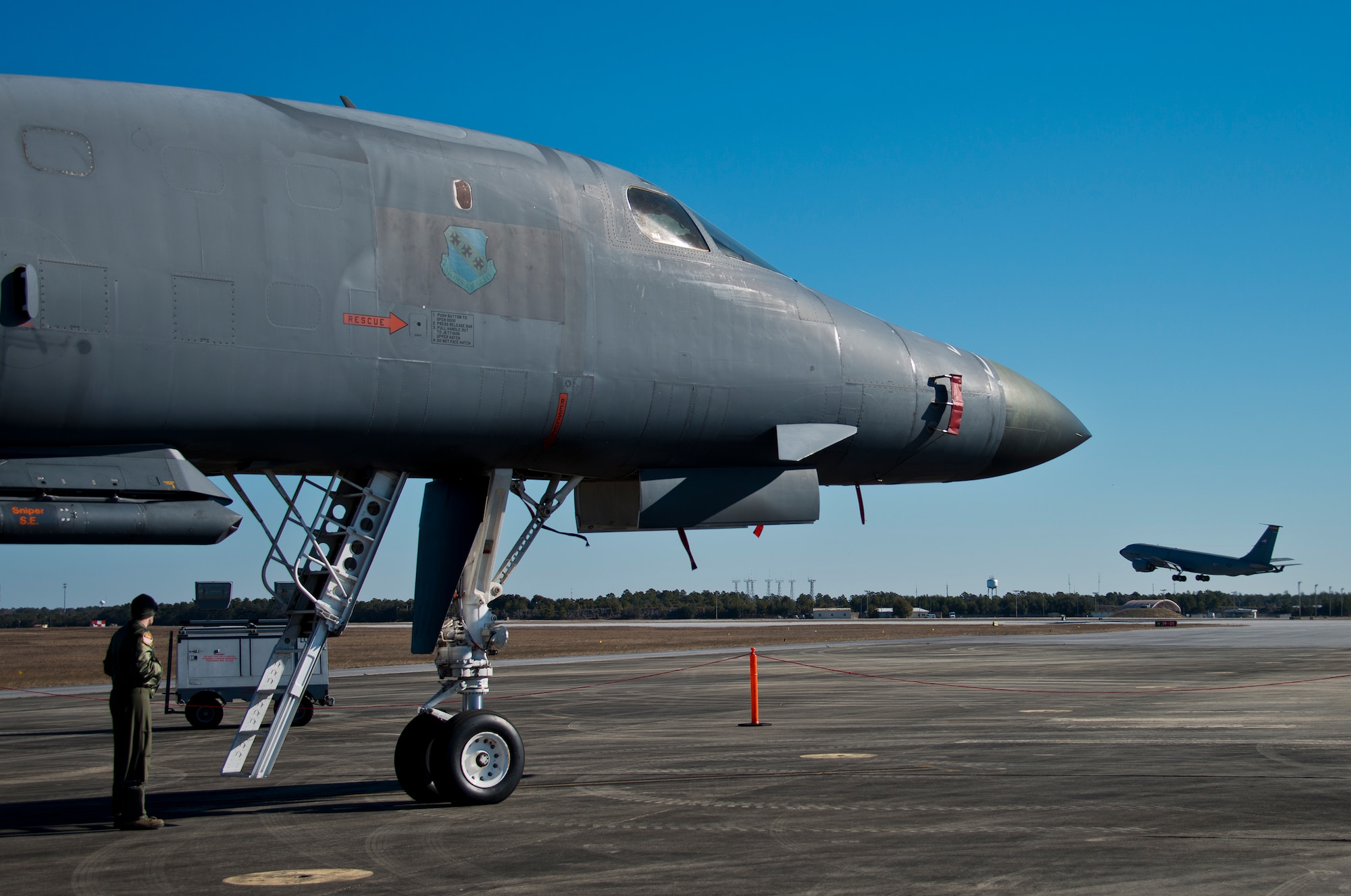 Capt. Curtis Michael, 337th Test and Evaluation Squadron, stands under a B-1B Lancer as a KC-135 Stratotanker lifts off from the runway at Eglin Air Force Base, Fla., Feb. 19. The 53rd Wing bomber from Dyess AFB, Texas was here for a few missions and to allow wing personnel an opportunity to see one of their geographically separated aircraft up close.  (U.S. Air Force photo/Samuel King Jr.)