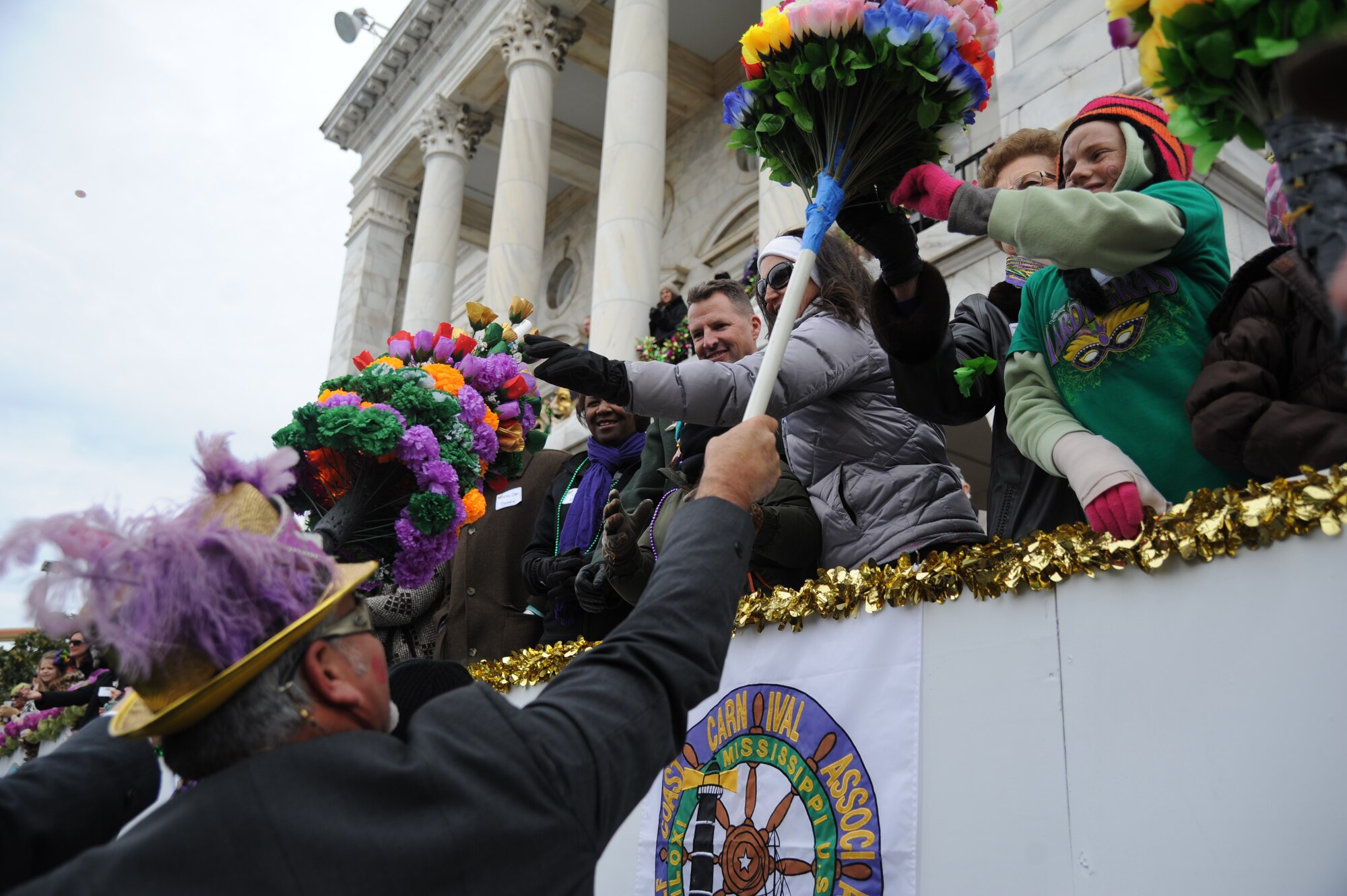 Brig. Gen. Patrick Higby, 81st Training Wing commander; his wife, Heather, and daughter, Hannah, accept a paper flower during the Gulf Coast Carnival Association Mardi Gras parade Feb. 17, 2015, in Biloxi, Miss.  The Keesler Honor Guard led the parade and other base leadership also attended the event.  (U.S. Air Force photo by Kemberly Groue)