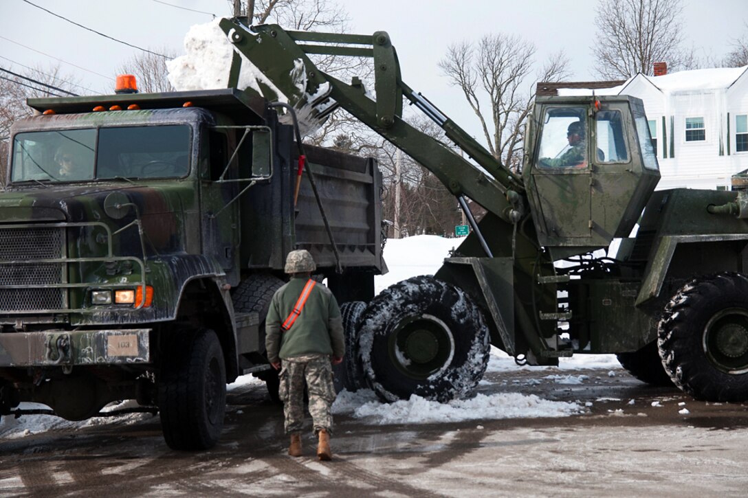 Army National Guard Spc. Jonathan Melanson dumps snow from his front end loader into a military dump truck during snow removal operations in Weymouth, Mass., Feb. 21, 2015. Melanson is a concrete and asphalt equipment operator assigned to the Massachusetts National Guard's 189th Engineer Company, 181st Engineer Battalion.