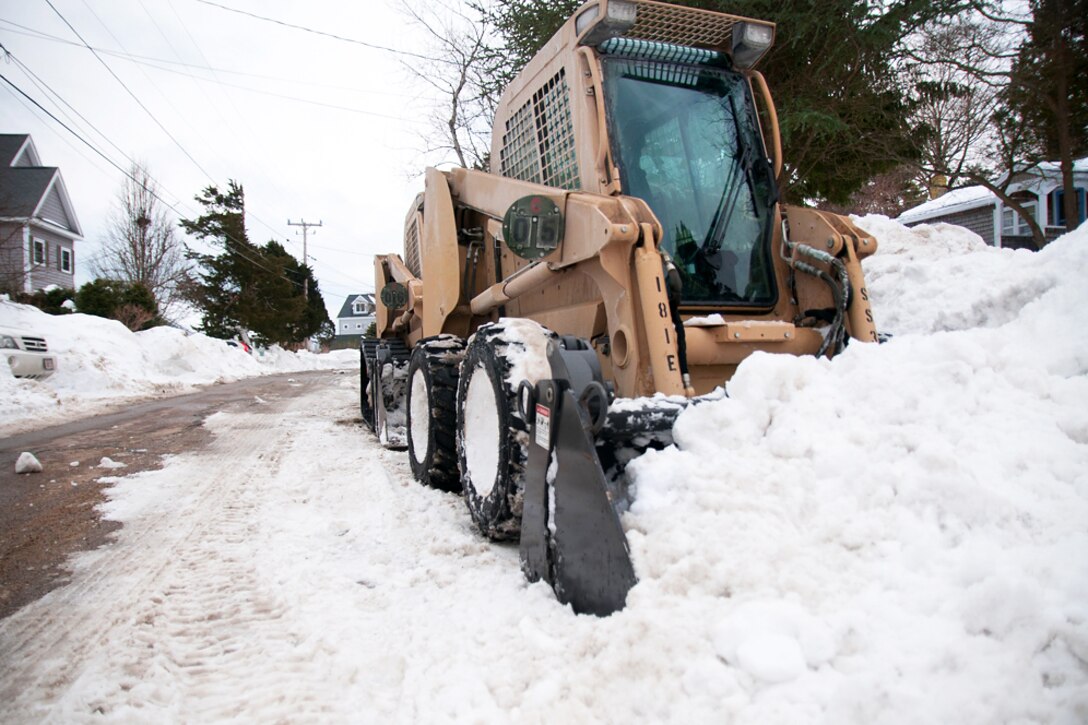 Soldiers operate skid steers to clear snow from a narrow road in Kingston, Mass., Feb. 21, 2015.