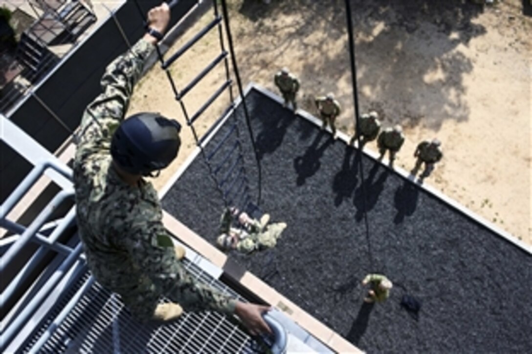 Navy Petty Officer 1st Class Robert Medina observes a sailor climbing a ladder during helicopter rope suspension training in San Diego, Feb. 17, 2015. The petty officer is an aircrew survival equipmentman assigned to Explosive Ordnance Disposal Training Evaluation Unit 1.