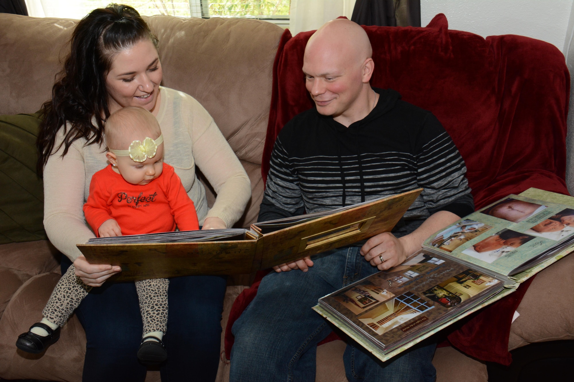 Staff Sgt. Richard L. Johnson and his wife, Christa, look at two scrapbooks with their daughter, Ayda, inside their home Feb. 13, 2014, in California. Christa designed the scrapbooks to document Richard’s seven-month long fight against cancer. Now cancer free, Richard said he feels blessed and he’s looking forward to getting back to work. Johnson is a 660th Aircraft Maintenance Squadron KC-10 crew chief. (U.S. Air Force photo/Tech. Sgt. James M. Hodgman)