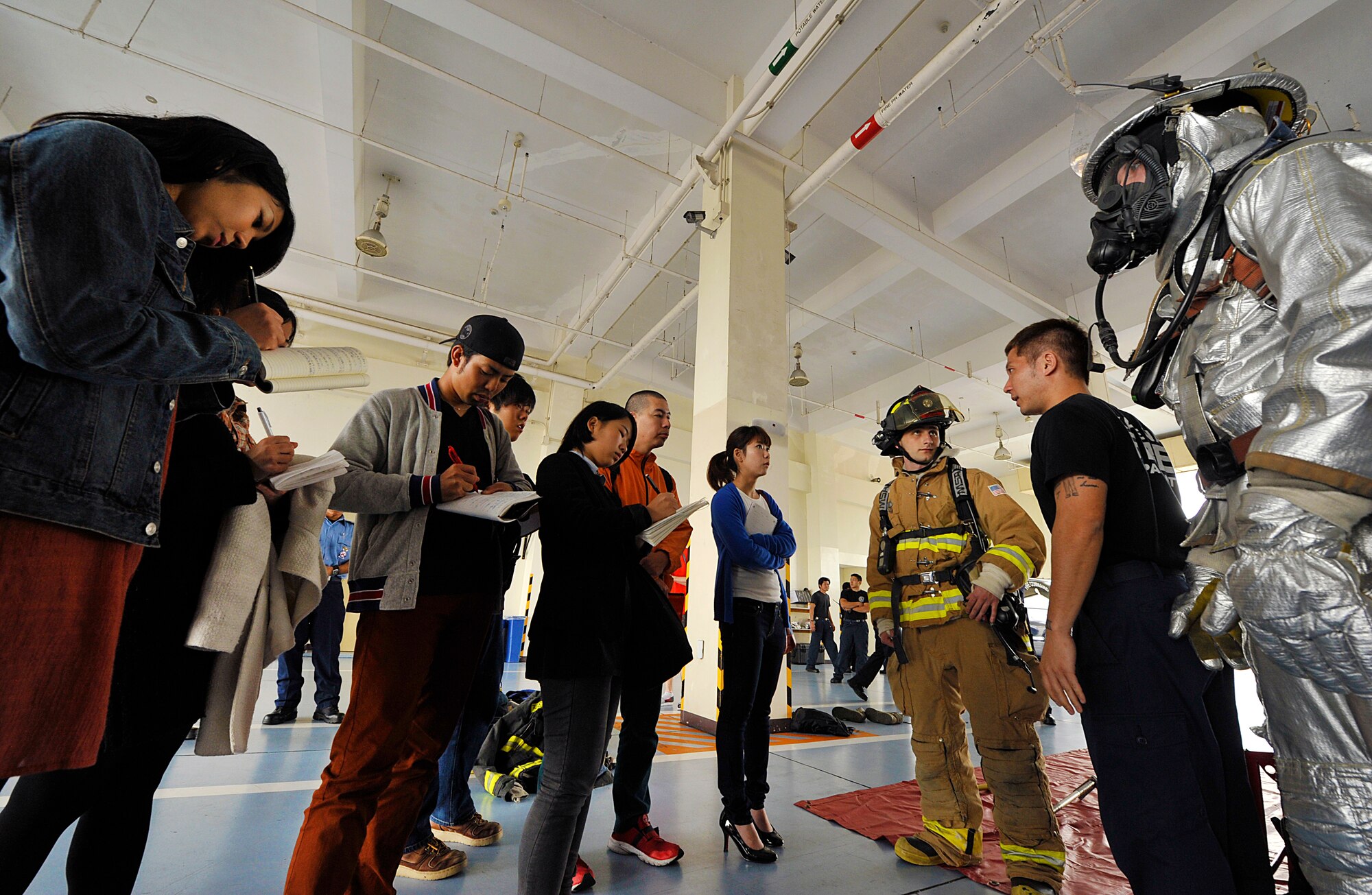 Students from the Okinawa International University take notes while Hideichiro Nakamura, 18th Civil Engineer Squadron fire fighter, explains the different use of bunker gear during their base visit to Kadena Air Base, Japan, Feb. 23, 2015. Six students and their instructors visited Kadena Air Base to learn about the U.S. military's response procedures and measures in case of typhoon and fire. (U.S. Air Force photo by Naoto Anazawa)