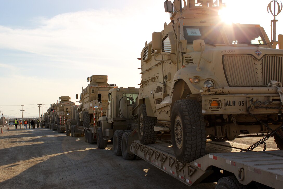 U.S., Afghan soldiers and contractors watch as a comvoy of trucks loaded with mine-resistant ambush protected vehicles are ready to be transfered over to the Afghan National Security Forces on Bagram Airfield, Afghanistan, Feb.14, 2015.