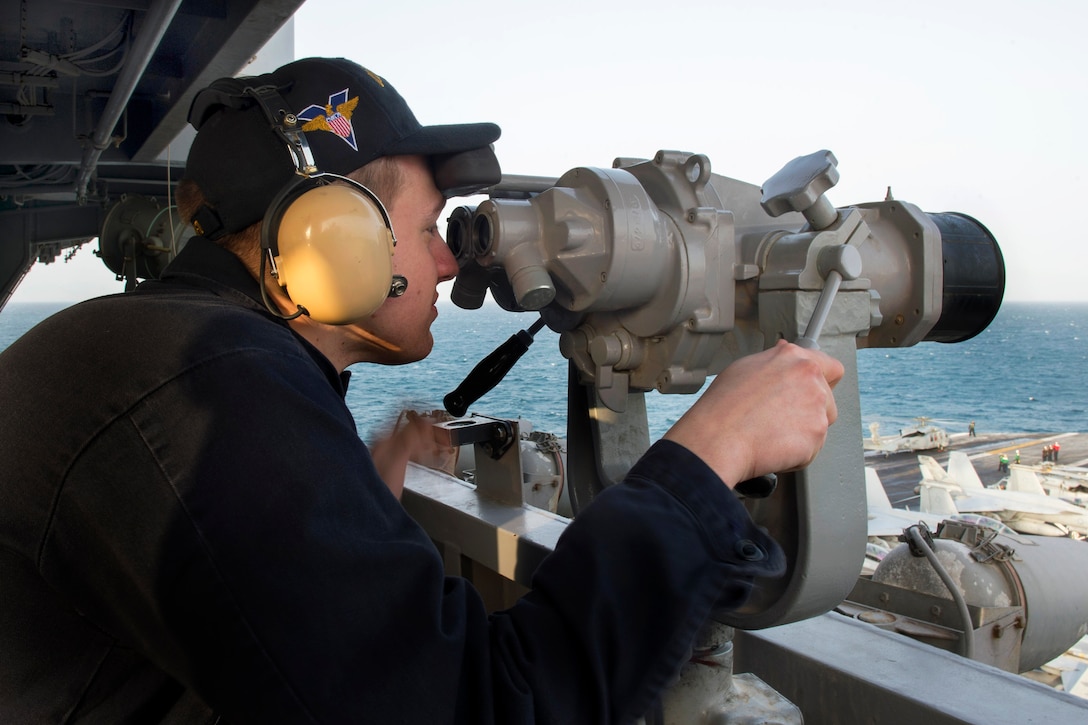 U.S. Navy Seaman Andrew Thompson uses high-powered binoculars to scan the horizon during a replenishment aboard the aircraft carrier USS Carl Vinson in the U.S. 5th Fleet area of responsibility, Feb. 18, 2015. Thompson is an operations specialist. 