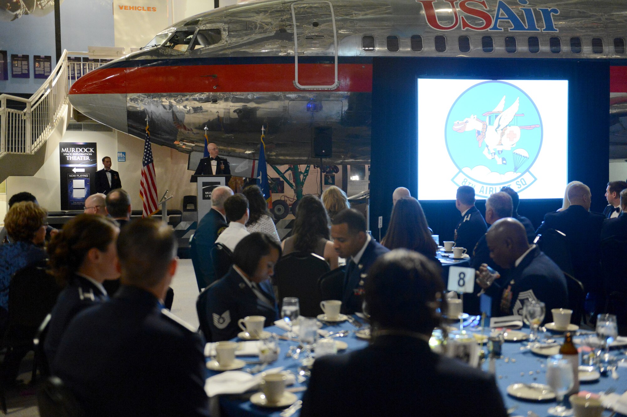 Lt. Col. William McDonald, 8th Airlift Squadron commander, talks about the squadron patch Feb. 19, 2015, during the 8th Airlift Squadron’s 75th anniversary at Boeing’s Museum of Flight Seattle, Wash. McDonald talked about the changes made to the 8th AS patch throughout its history and spoke about the meaning of it. The patch contains a winged workhorse, branded at the hip with a red cross. (U.S. Air Force photo/Airman 1st Class Keoni Chavarria)
