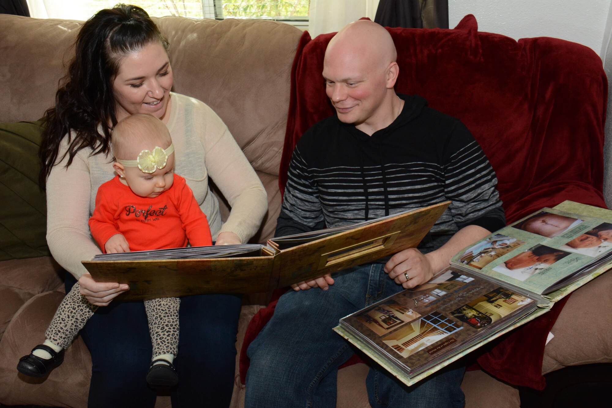 Staff Sgt. Richard L. Johnson and his wife, Christa, look at two scrapbooks with their daughter, Ayda, inside their home Feb. 13, 2014, in California. Christa designed the scrapbooks to document Richard’s seven-month-long fight against cancer. Now cancer free, Richard said he feels blessed and he’s looking forward to getting back to work. Johnson is a 660th Aircraft Maintenance Squadron KC-10 crew chief. (U.S. Air Force photo/Tech. Sgt. James M. Hodgman)