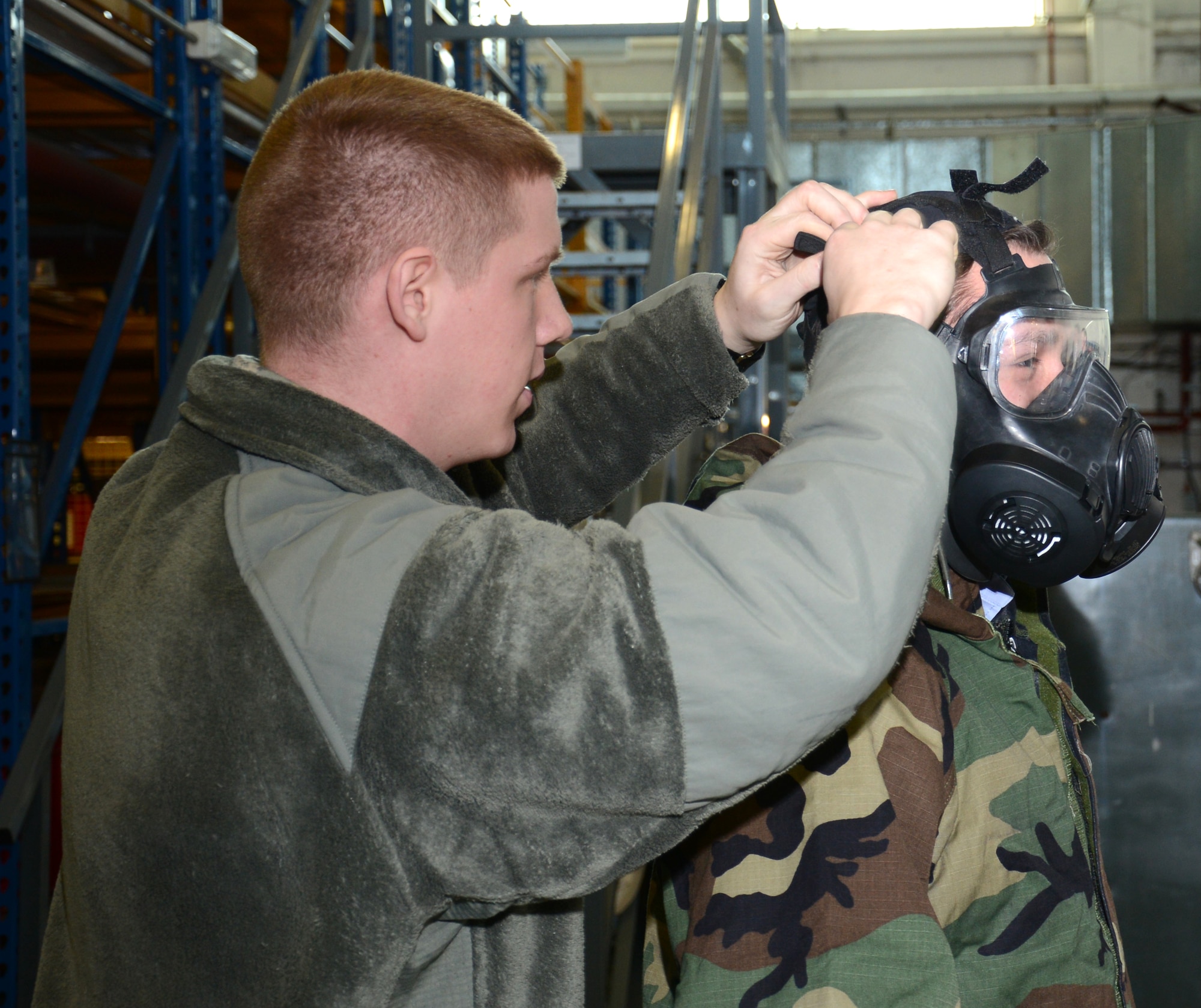 U.S. Air Force Airman 1st Class James Brewer, left, 100th Logistics Readiness Squadron Individual Protective Equipment mobility apprentice from Shawnee, Okla., assists Flying Officer Graham Macalister with a chemical gear gas mask demonstration Feb. 24, 2015, on RAF Mildenhall, England. Royal Air Force Logistics officers visited with members of the 100th LRS during a site tour to further improve relations between the two nations. (U.S. Air Force photo by Gina Randall/Released)