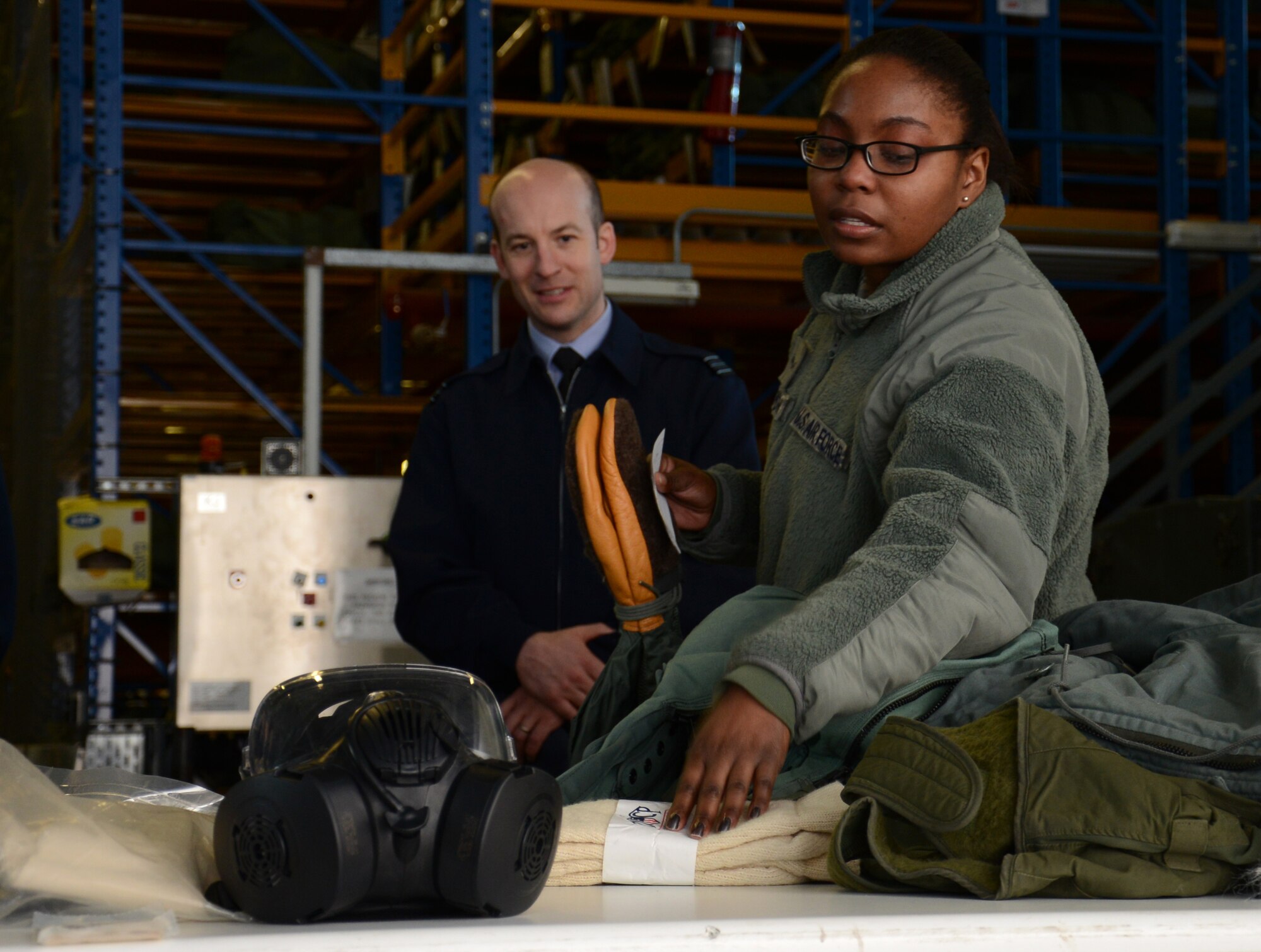 U.S. Air Force Airman 1st Class Andrea Blackmon, right, 100th Logistics Readiness Squadron Individual Protective Equipment mobility apprentice from Miami, Fla., shows equipment and clothing to Royal Air Force Logistics officers during a tour of the LRS squadron Feb. 24, 2015, on RAF Mildenhall, England. Members of the RAF visited with members of the 100th LRS during a site tour to further improve relations between the two nations. (U.S. Air Force photo by Gina Randall/Released)