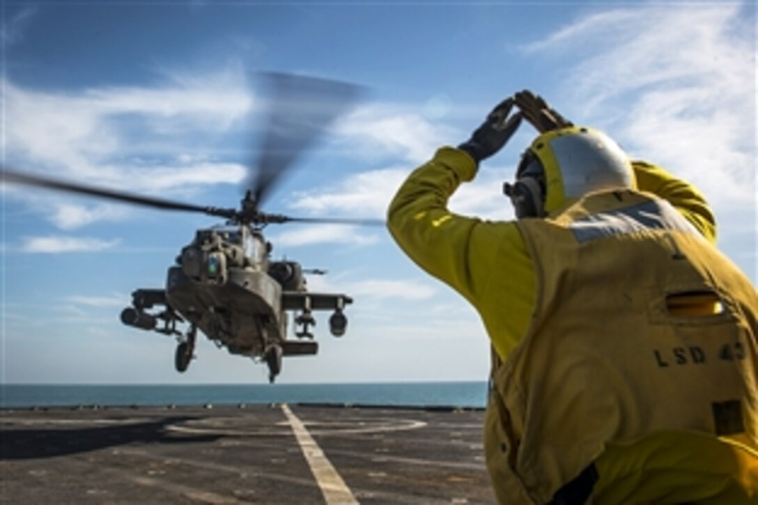 U.S. Navy Petty Officer 2nd Class Nicholas Ferris signals to an AH-64 Apache helicopter during deck landing qualifications aboard the amphibious dock landing ship USS Fort McHenry in the Arabian Gulf, Feb. 24, 2015. Ferris is a boatswain's mate.
