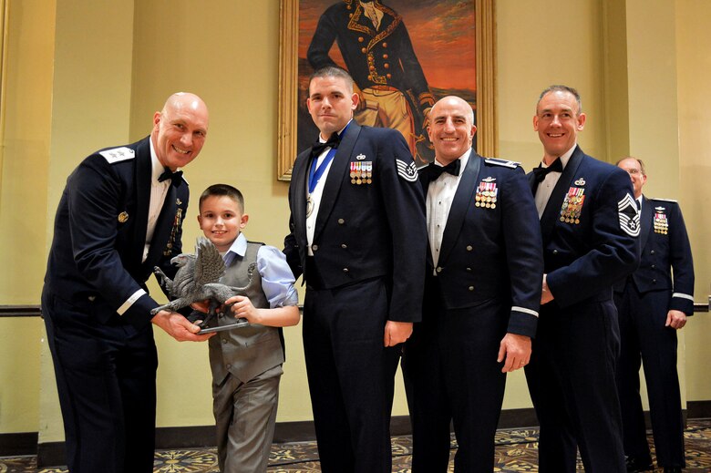 Maj. Gen. Timothy Zadalis, 618th Air Operations Center commander, presents the 43rd Airlift Group’s 2014 First Sergeant of the Year Gryphon trophy to Tech. Sgt. Brian Fisher, 3rd Aerial Port Squadron, and his son, Cody, 9, accepting on behalf of his spouse, Master Sgt. Rory Fisher, 43rd Airlift Group, who is currently deployed, with Col. Kenneth Moss, 43rd Airlift Group commander and Chief Master Sgt. James Cope, 43rd Airlift Group superintendent, during the 440th Airlift Wing and 43rd Airlift Group 2014 Annual Awards Banquet held at the Fort Bragg Club, Feb. 21, Fort Bragg, N.C. (U.S. Air Force photo/Marvin Krause)