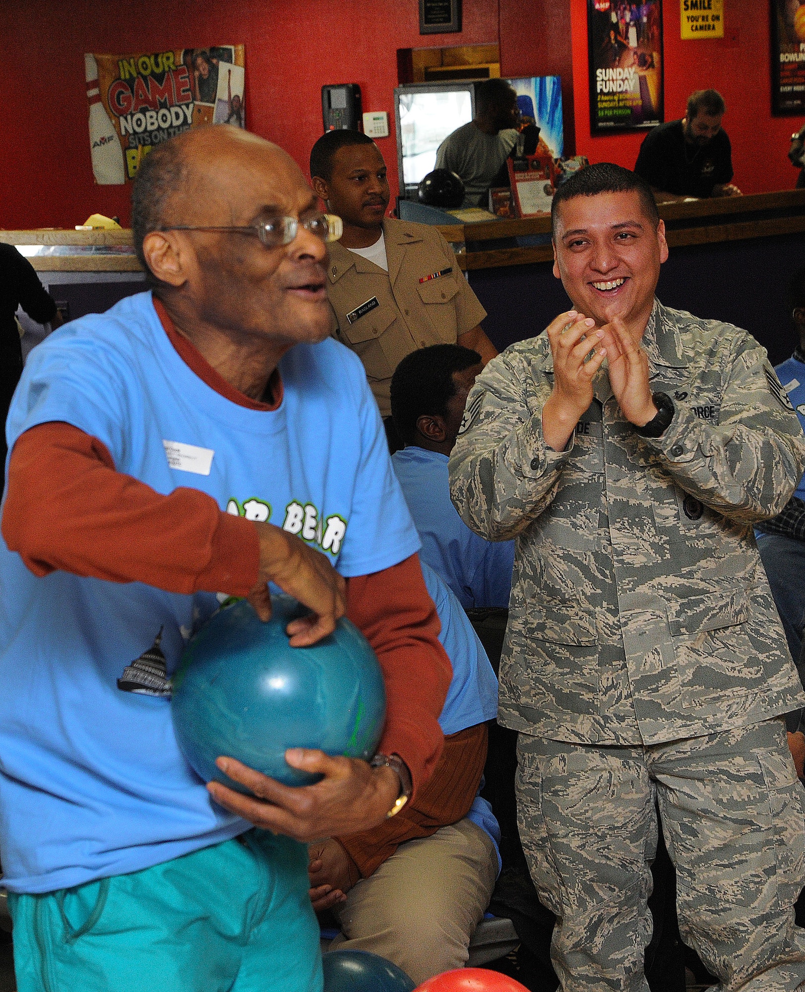 Athlete Paul Cook approaches a bowling lane as Staff Sgt. Daniel Andrade cheers him on during the D.C. Special Olympics Bowling Championship Feb. 25, 2015, in Hyattsville, Md. Cook is 80 years old and really enjoys these types of events. More than 50 Airmen showed up to assist athletes while they bowled. Andrade works a clerk at Pass & Registration for the 11th Security Support Squadron, Joint Base Andrews. (U.S. Air Force photo/James E. Lotz) 